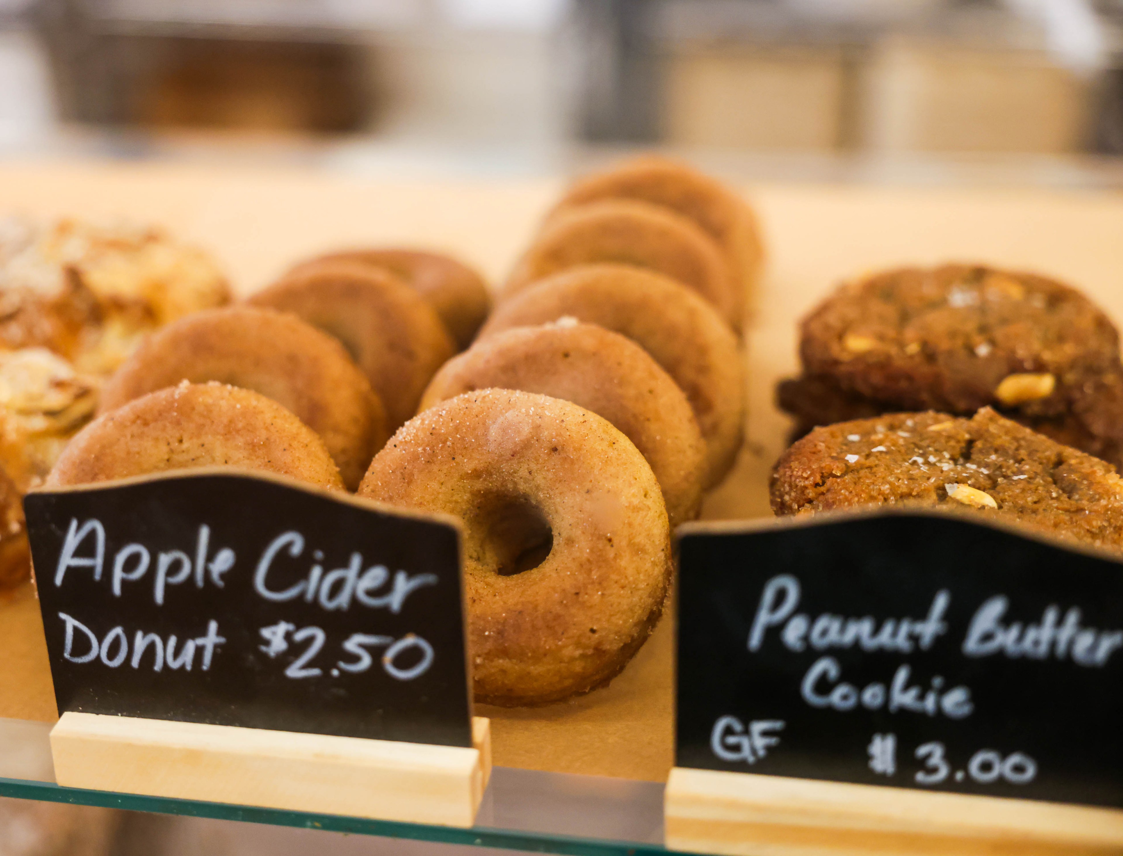 Apple cider donuts next to peanut butter cookies with prices on small chalkboard signs.
