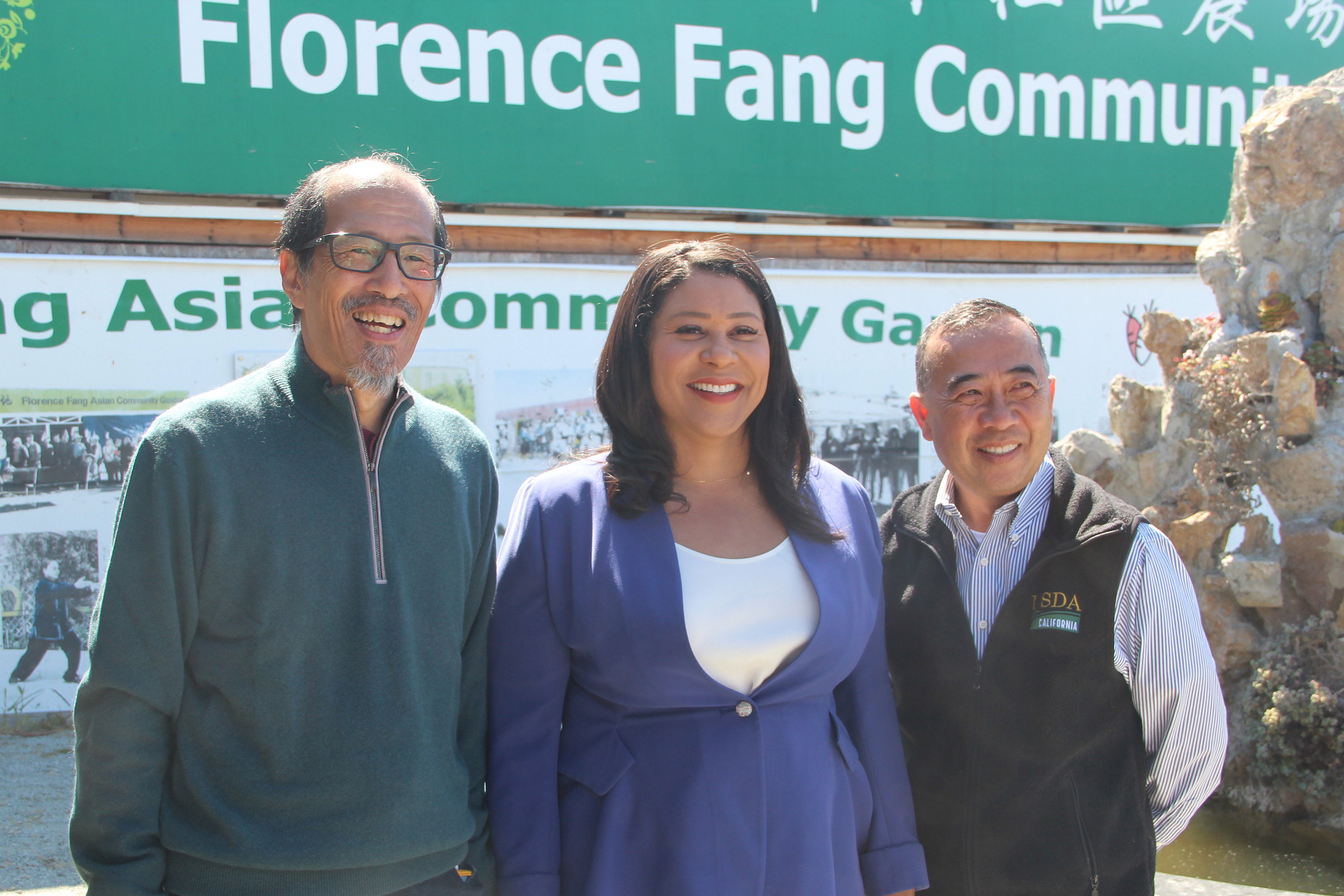 Three people are smiling in front of a sign for the Florence Fang Community Garden.