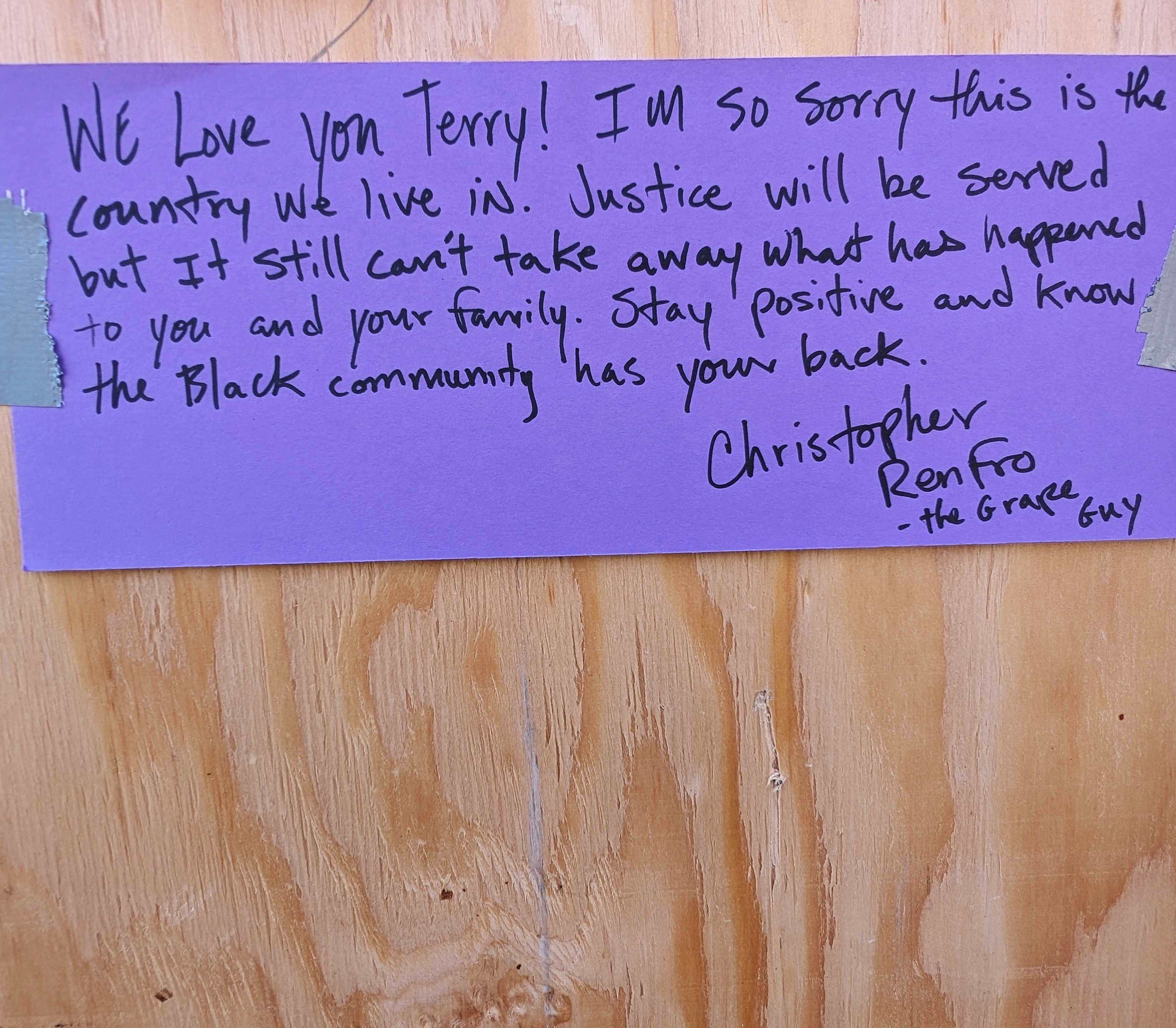 A handwritten message on purple paper, taped to a wooden surface, expresses support for a person named Terry and mentions justice and community solidarity.