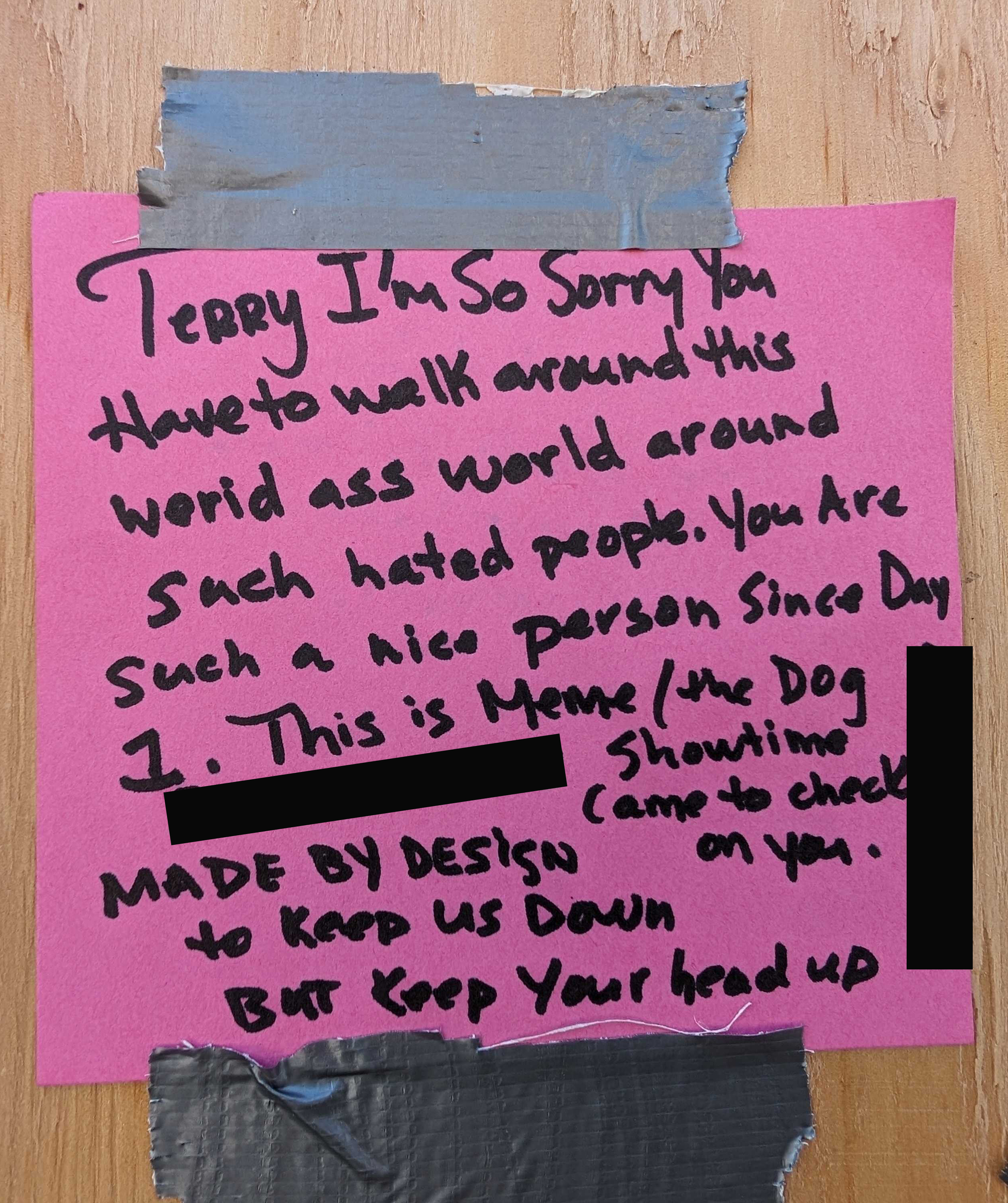 A handwritten note on a pink paper is taped to a wooden surface with duct tape. The note expresses sympathy and encouragement. Parts of the message are redacted.