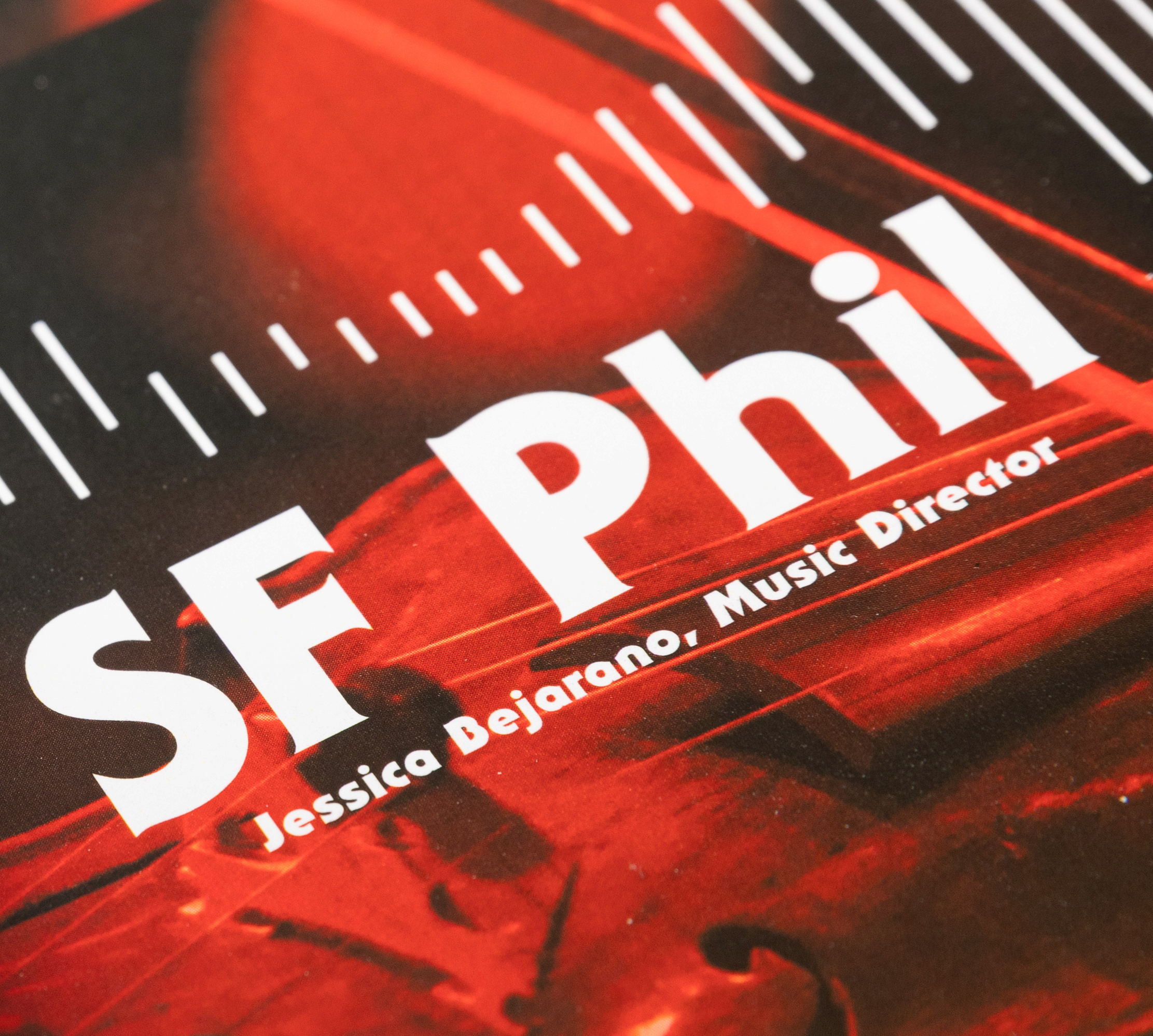 The image shows a red-toned promotional poster with the bold white text &quot;SF Phil&quot; and &quot;Jessica Bejarano, Music Director&quot; below it, featuring musical notes.