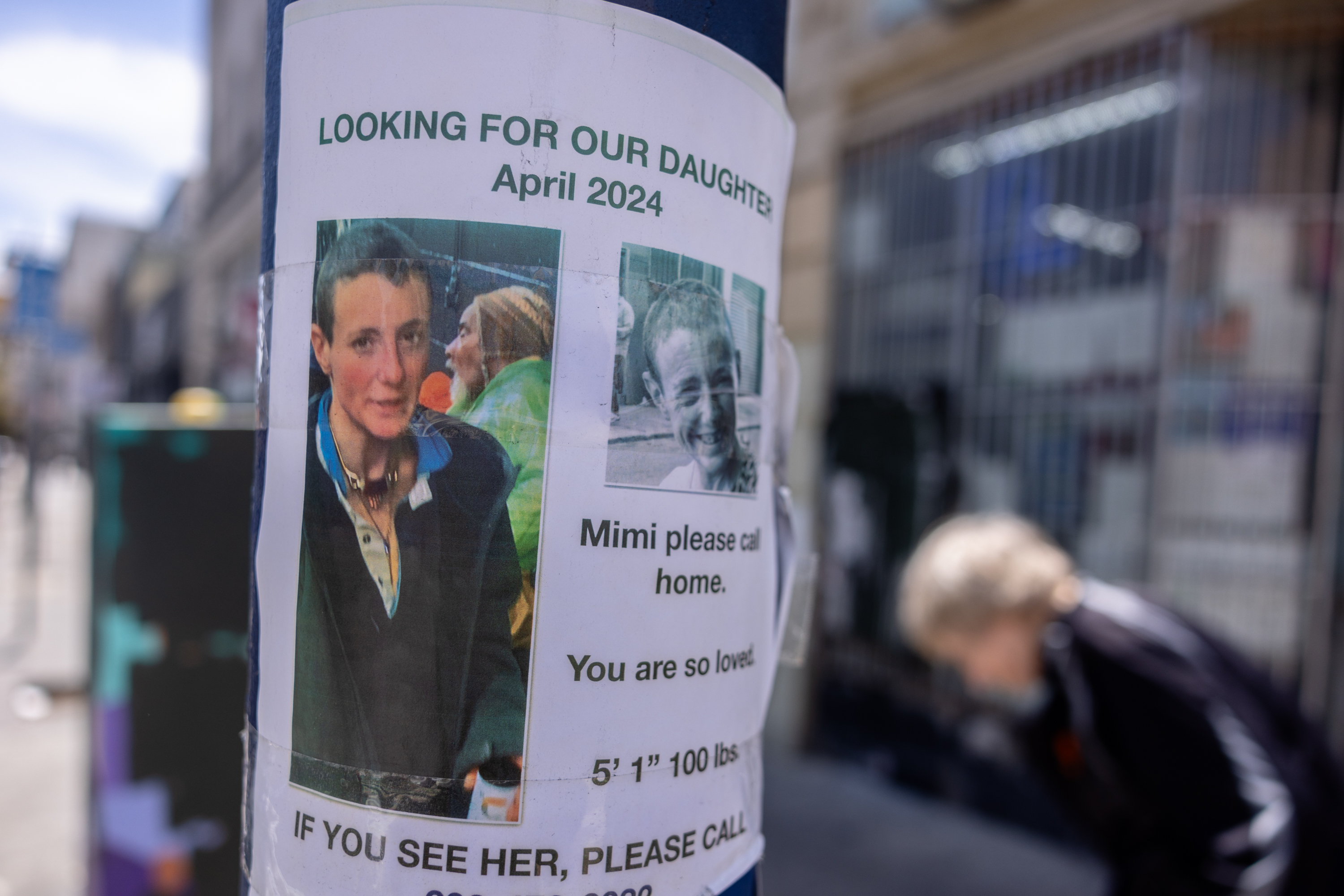 A missing daughter's poster is attached to a pole with photos and contact details.