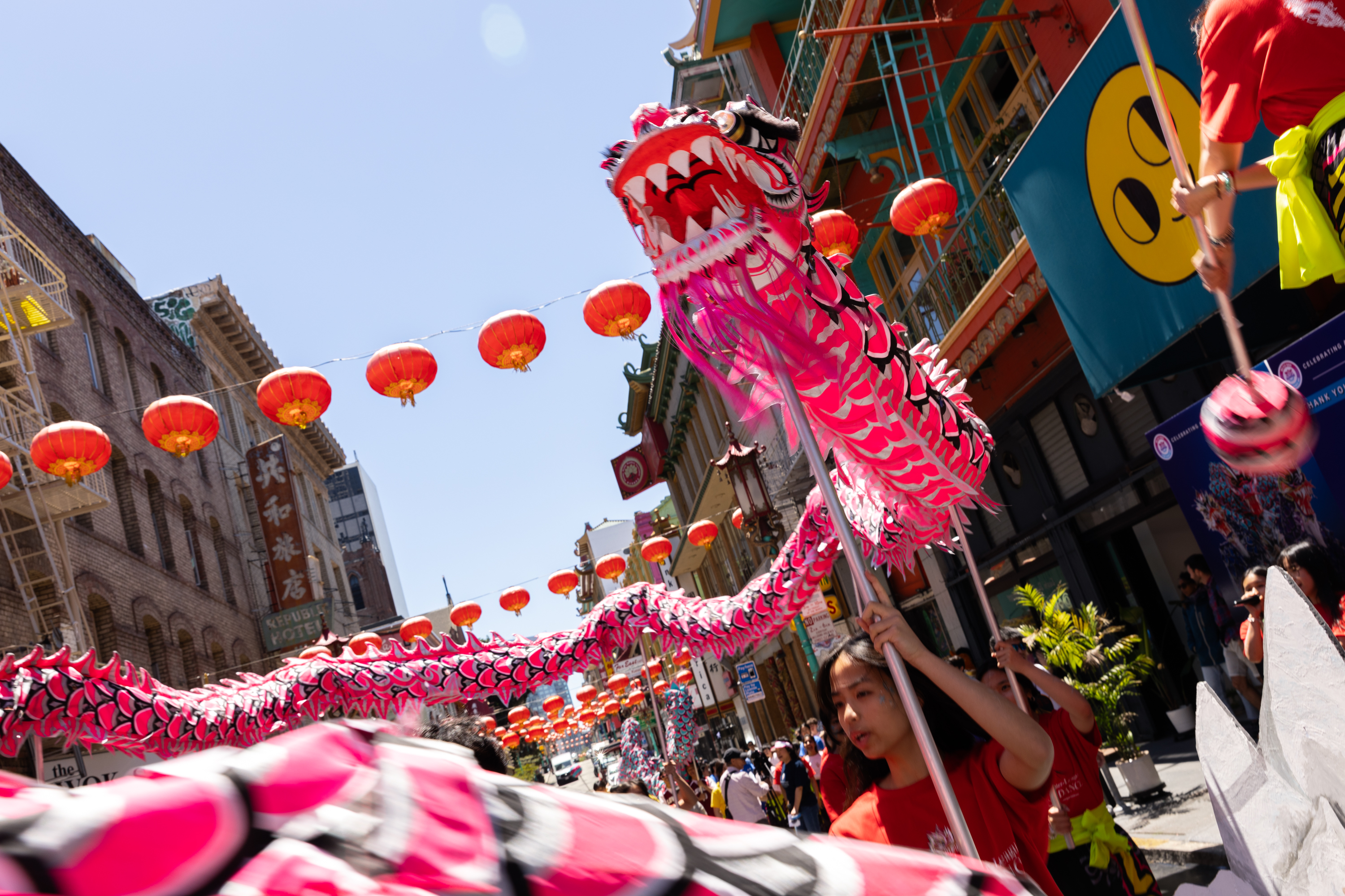 A bright dragon dance in a vibrant street with red lanterns above, performers in red partly visible.