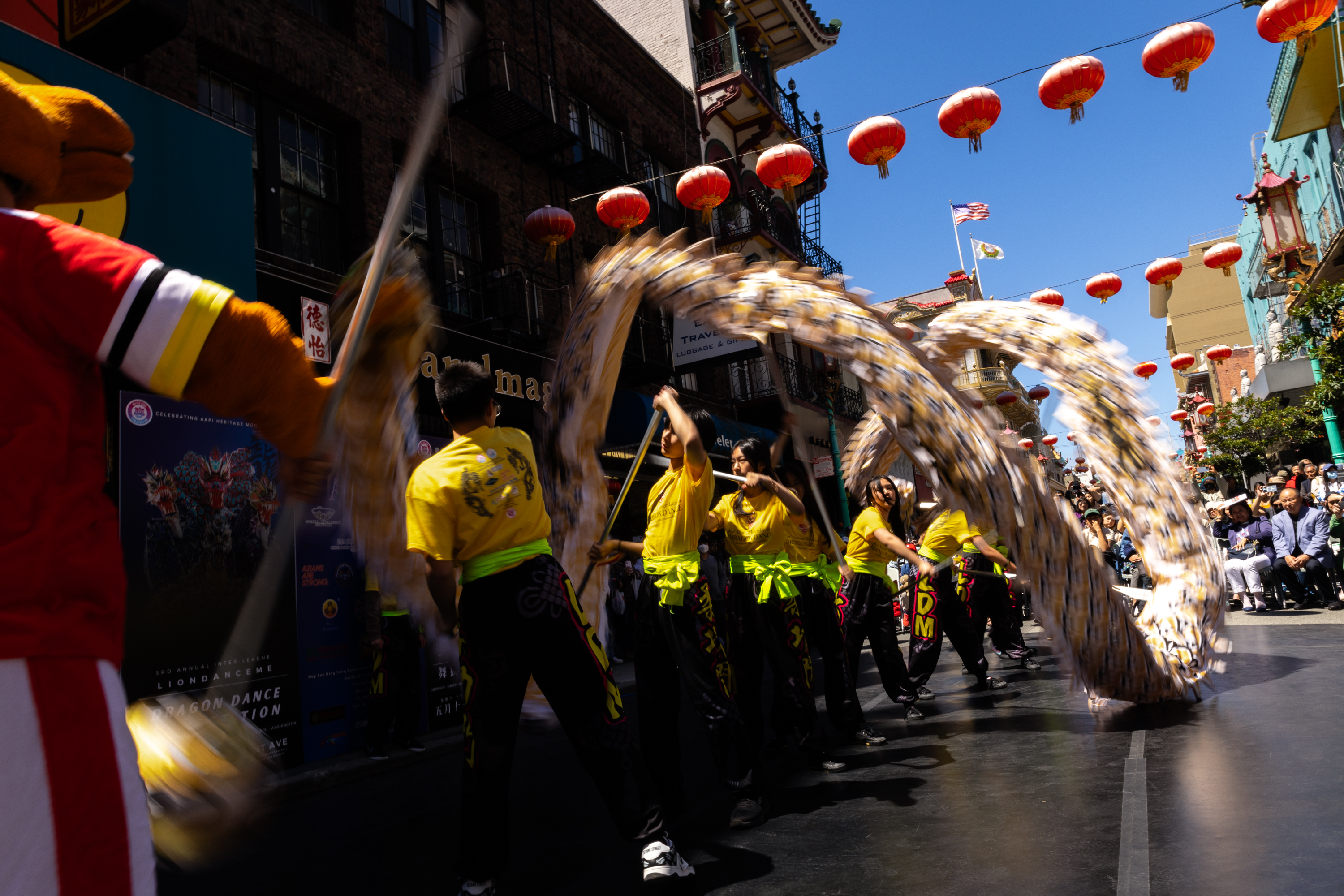 A dynamic street parade with performers in yellow dancing with long, flowing dragon costumes under red lanterns.