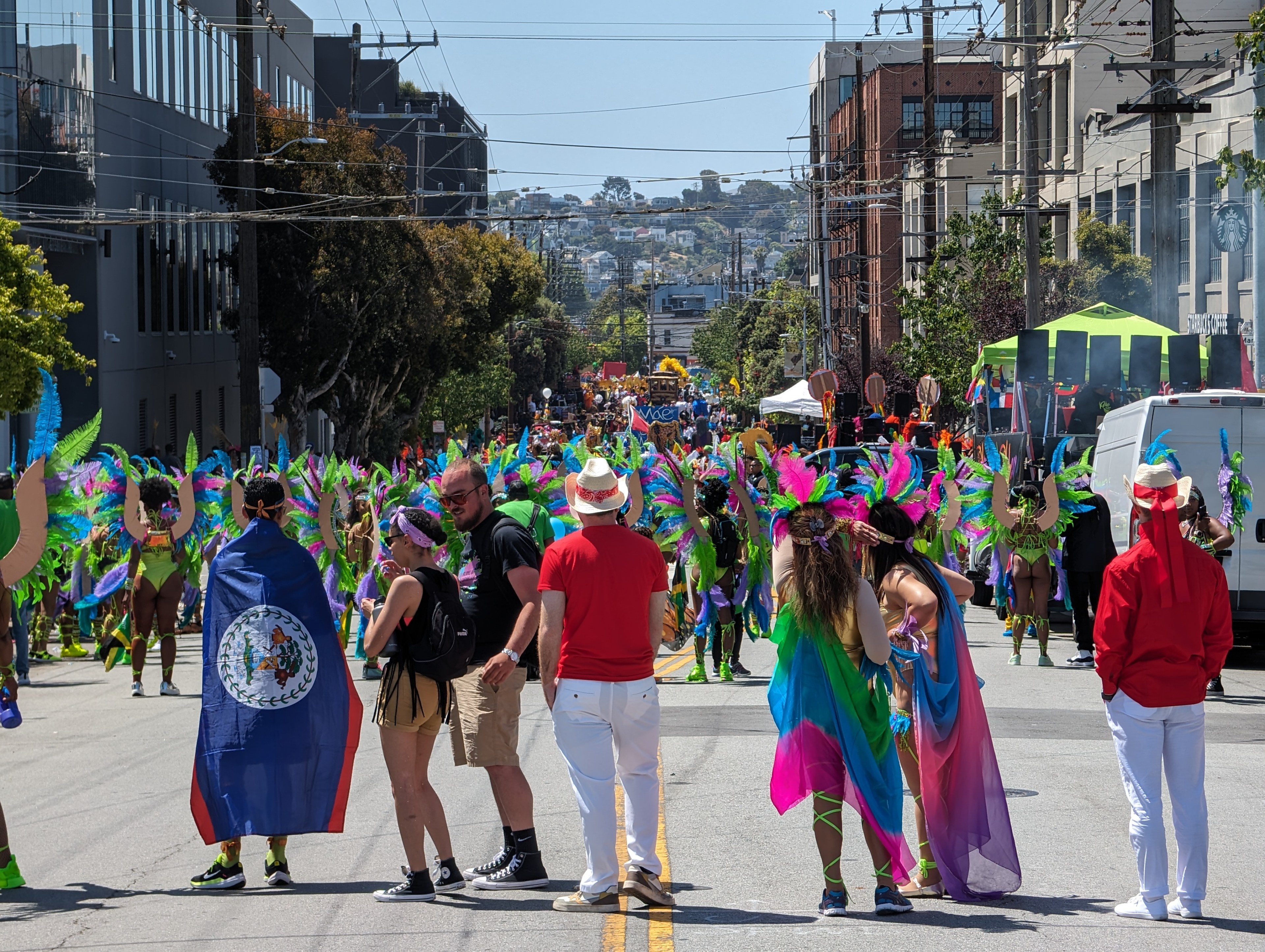 A group of eight people watch hundreds of other people wearing brightly colored outfits line several blocks of a city street during a parade.