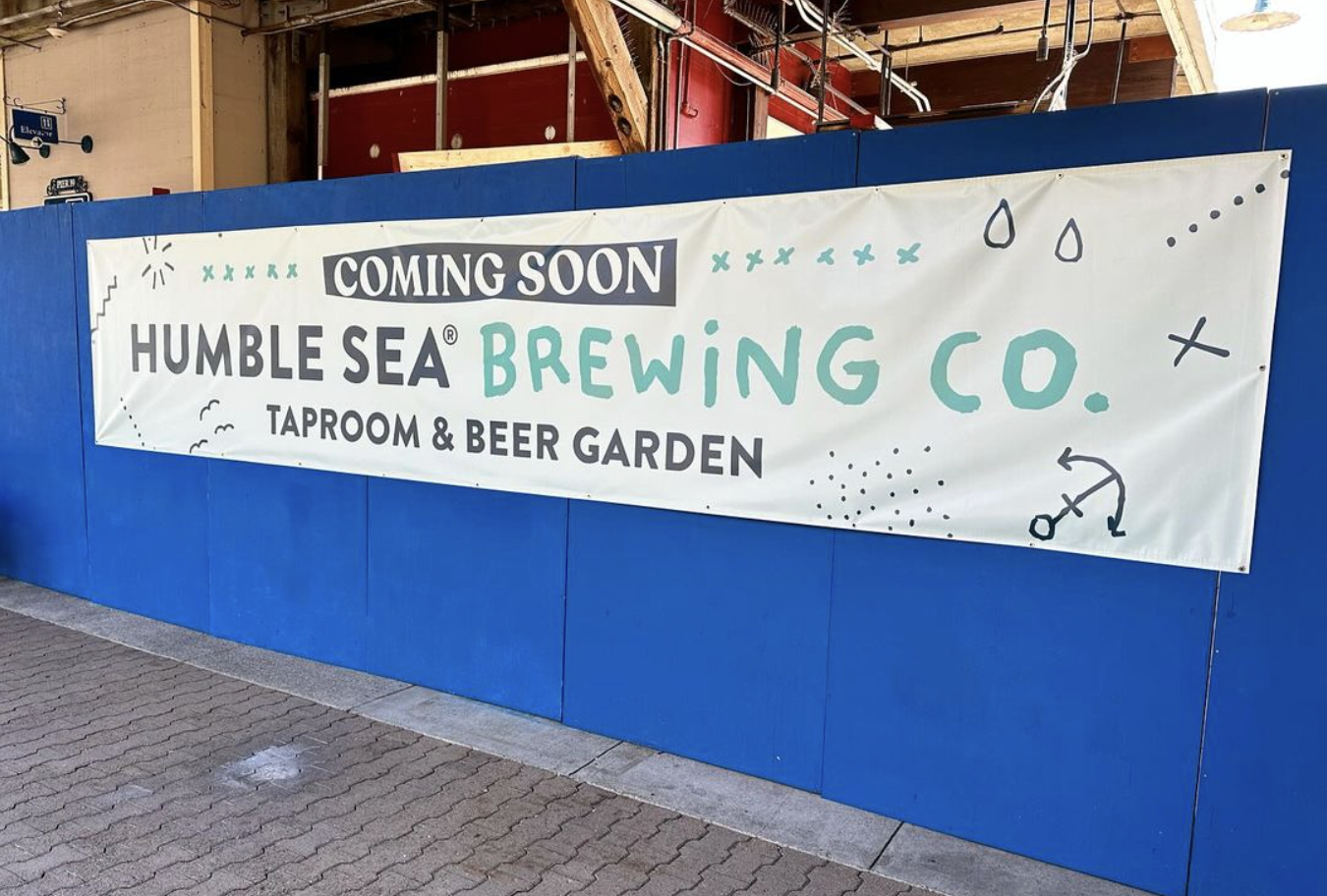 a banner teasing the opening of a craft brewery hangs on a wall in front of a construction site