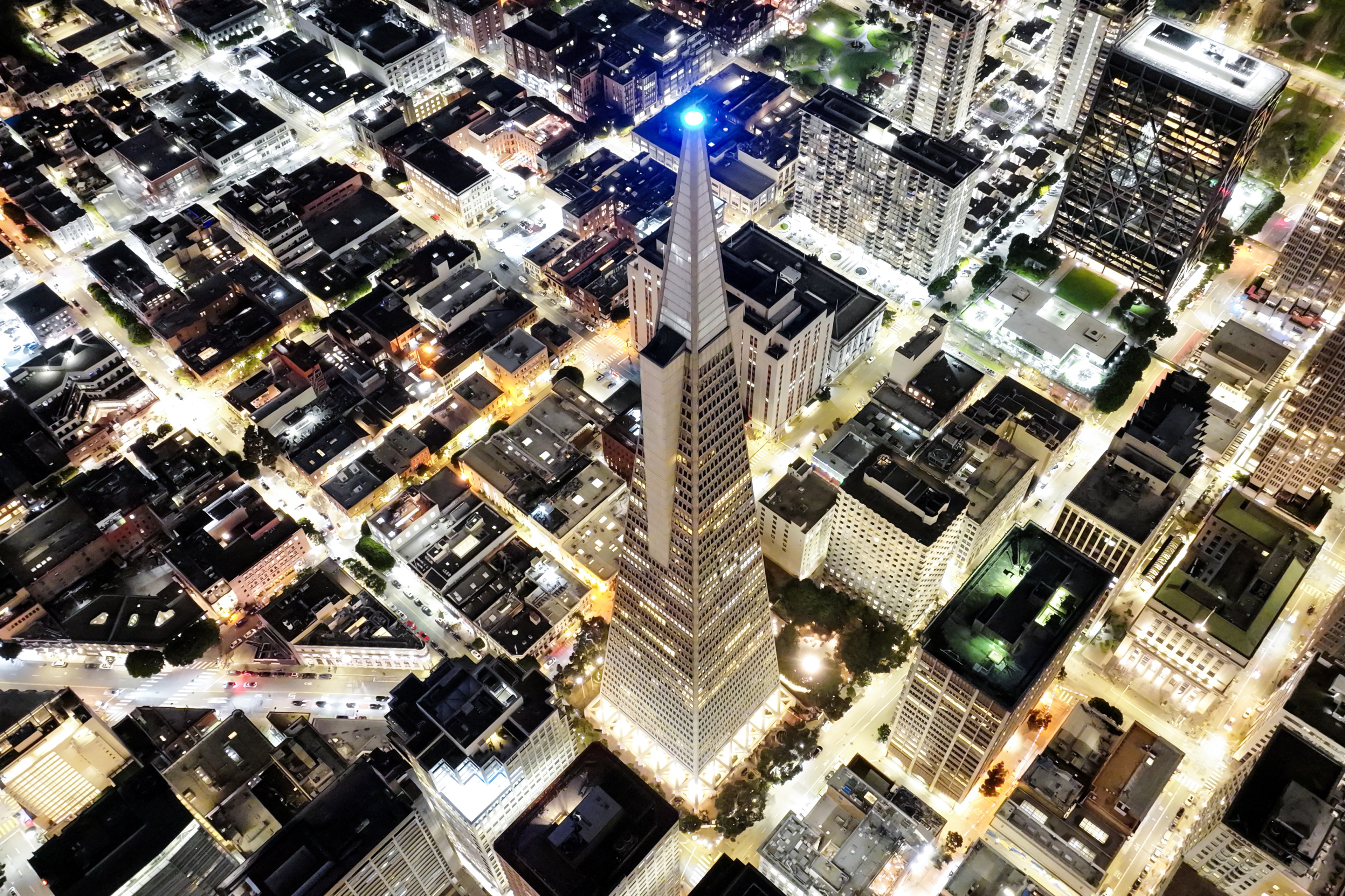 Aerial night view of a brightly lit city with a tall illuminated skyscraper at the center.