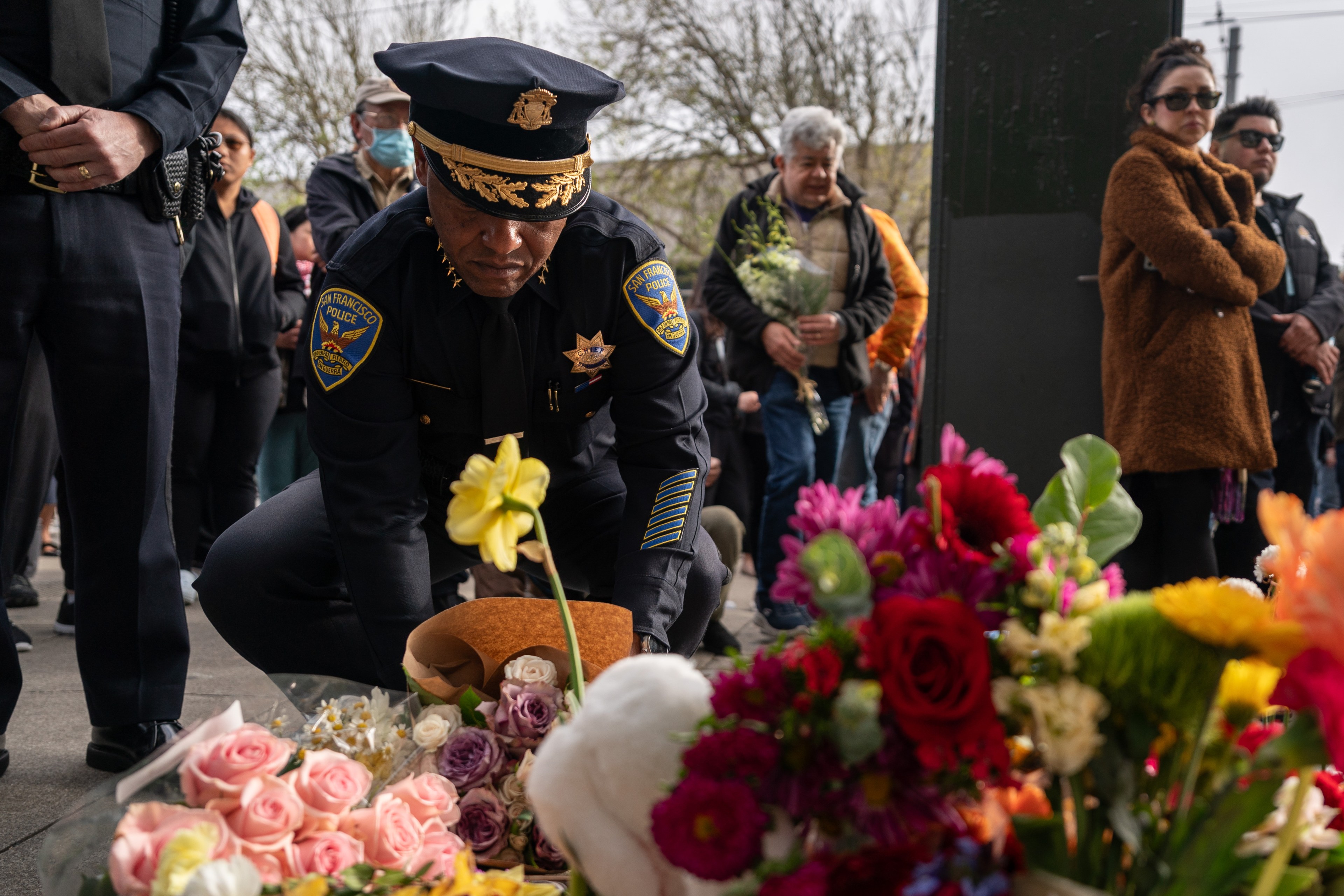 A police chief lays flowers on the ground in front of a crowd.