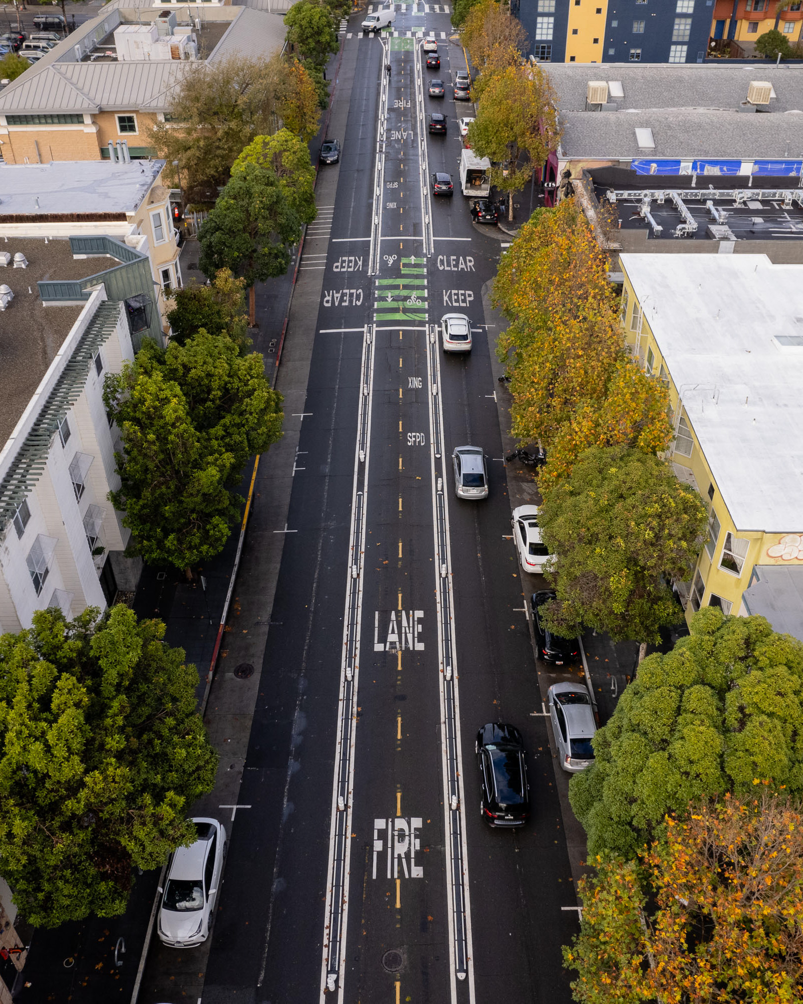 An aerial view of a street lined with trees and buildings shows a &quot;FIRE LANE&quot; with clear &quot;KEEP CLEAR&quot; markings, and cars parked on both sides.