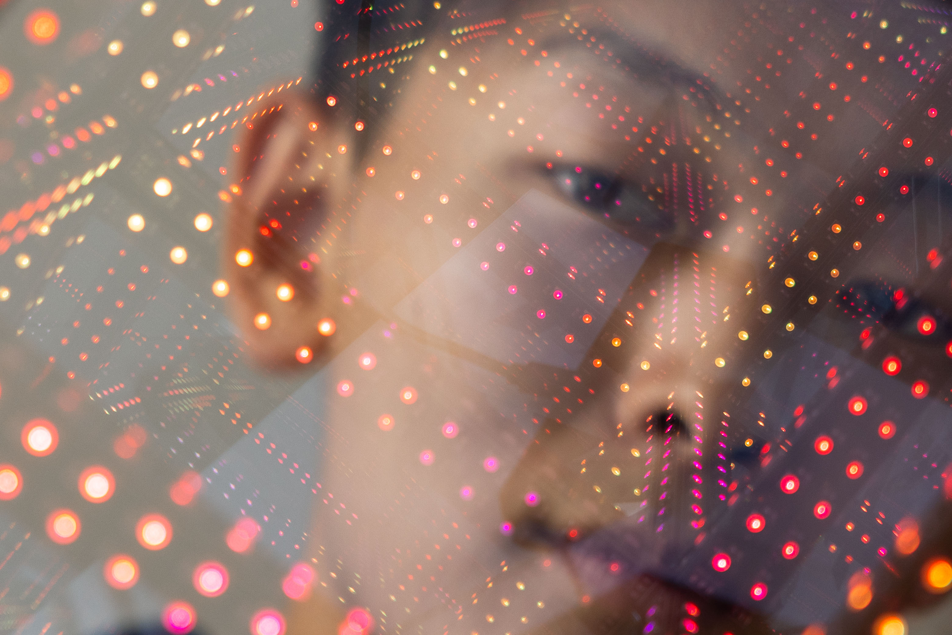 The image features a person's blurry face overlaid with a grid of bright, colorful LED lights, creating a futuristic and abstract effect.
