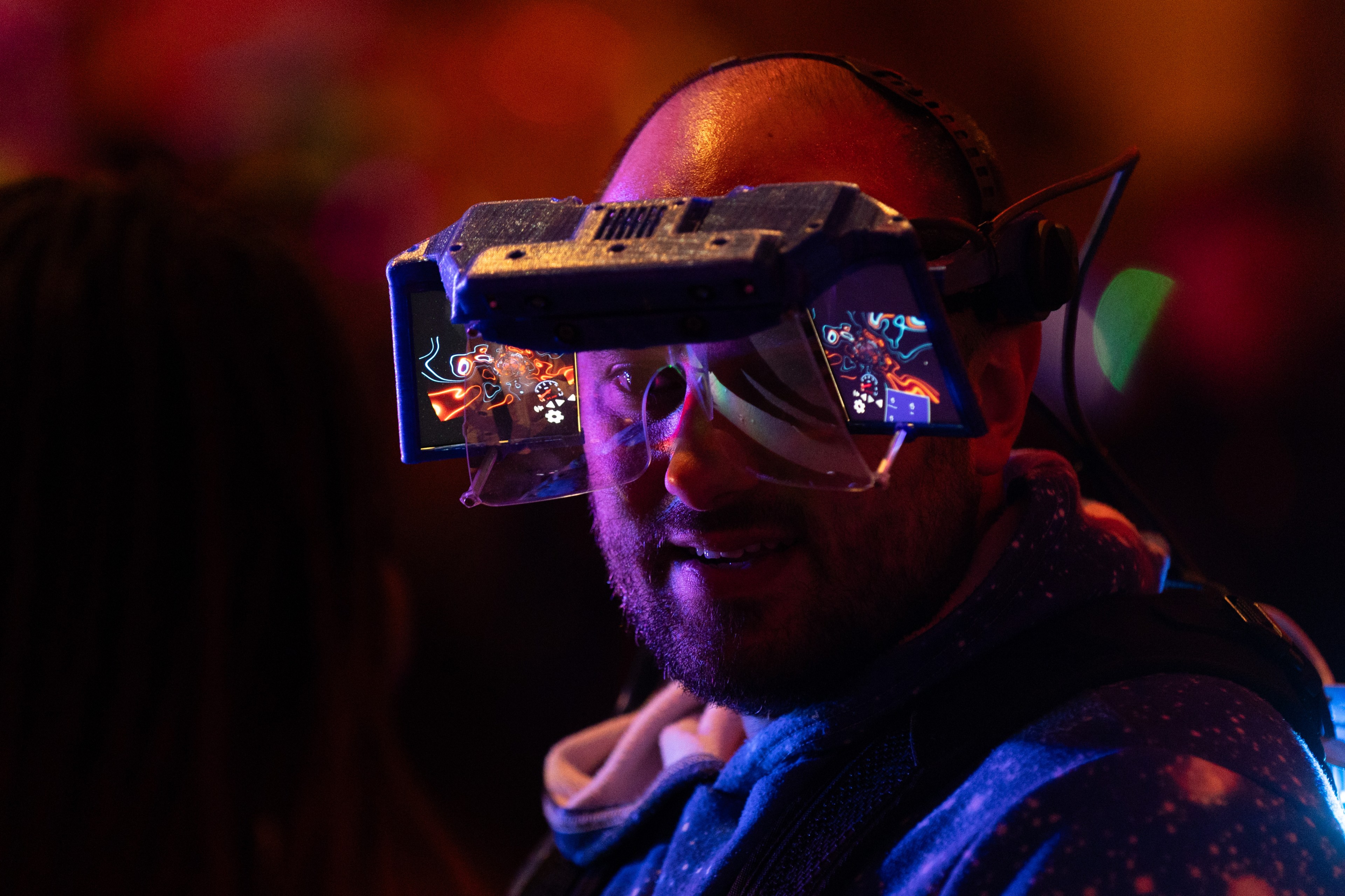 A person wearing futuristic, augmented reality glasses is depicted, with colorful graphics reflecting on the lenses, bathed in vibrant, multicolored lighting.