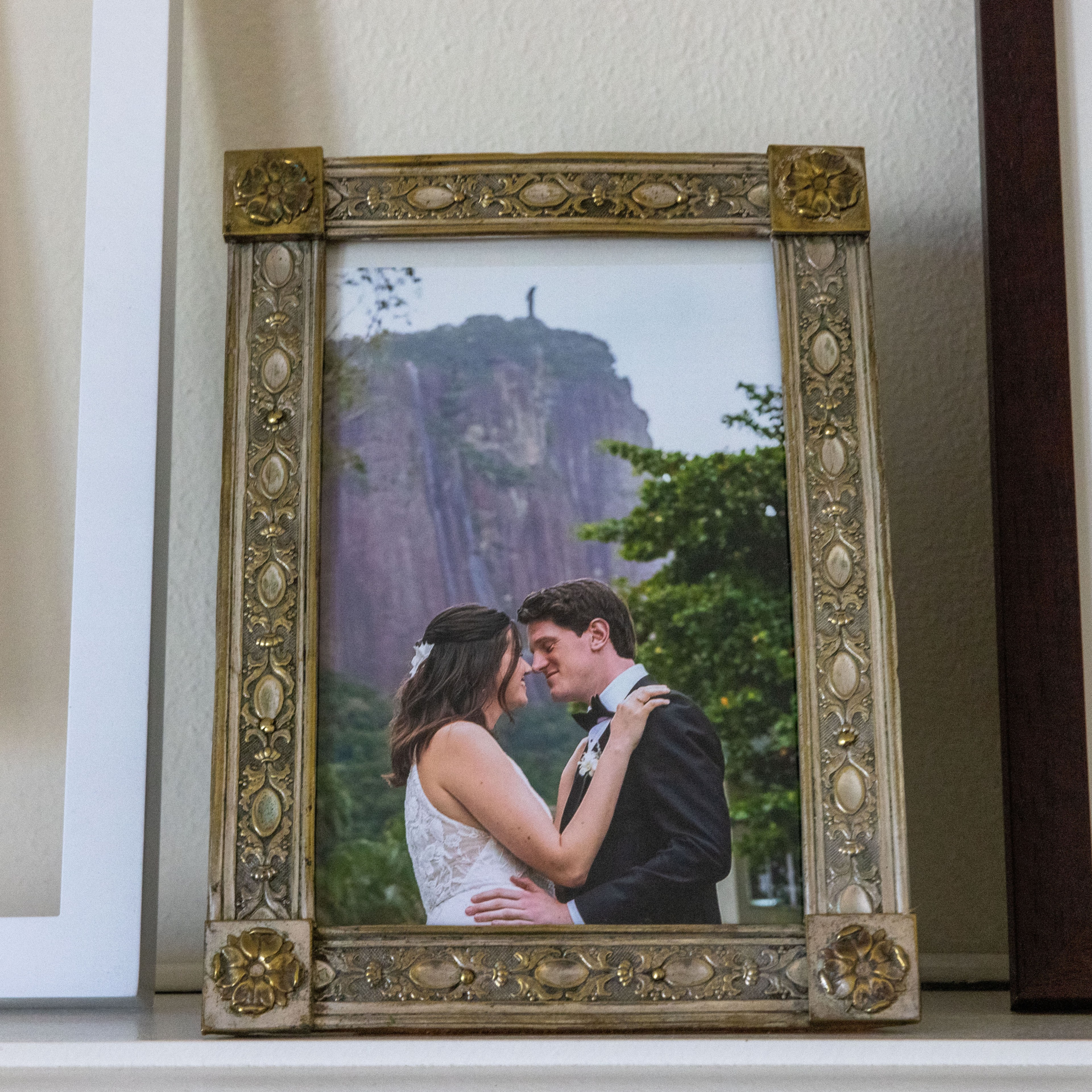 A framed photo shows a bride and groom embracing outside, with a large statue on a hill in the background. The ornate gold frame surrounds the image.