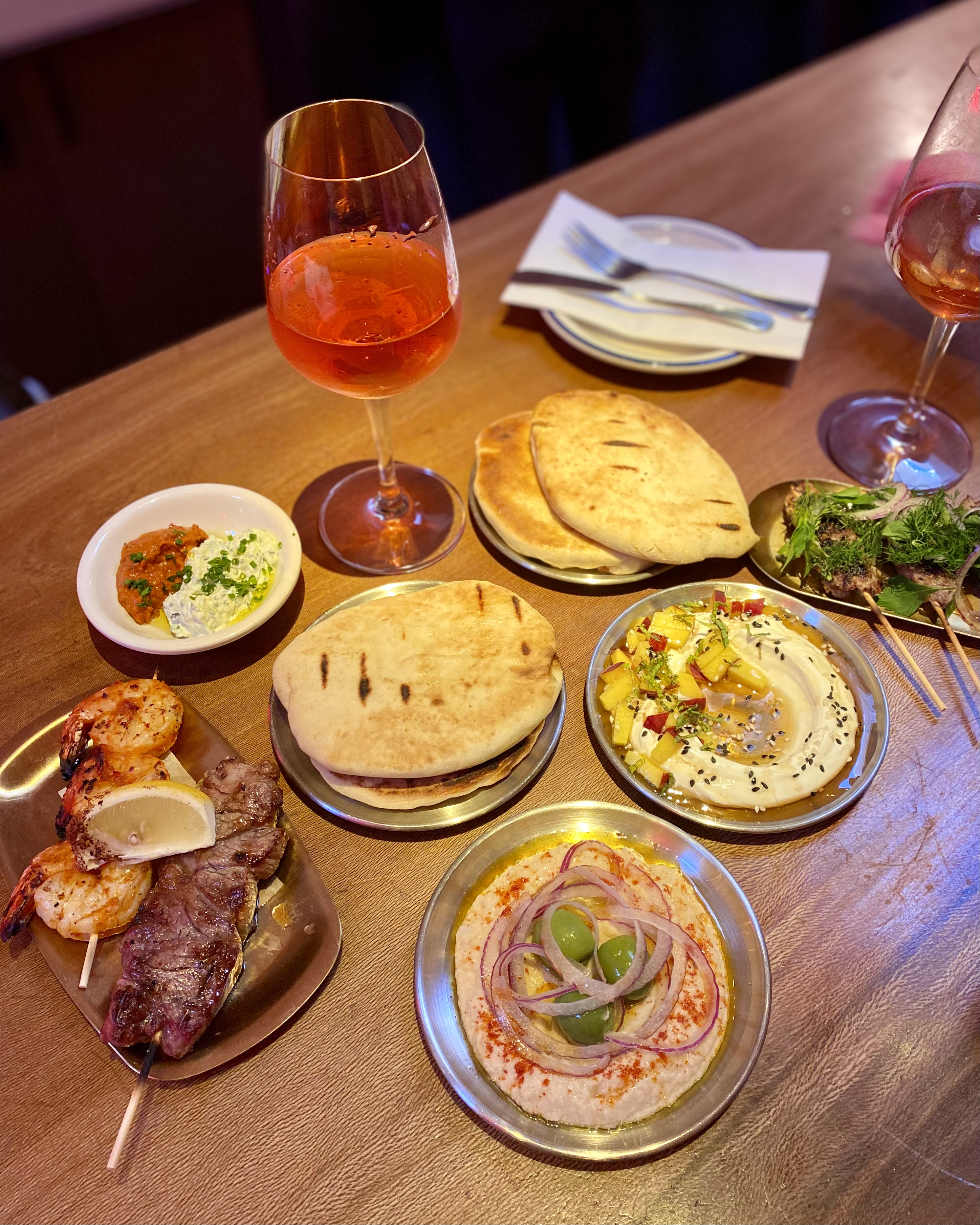 A selection of small plates on a wooden bar with two glasses of red wine.
