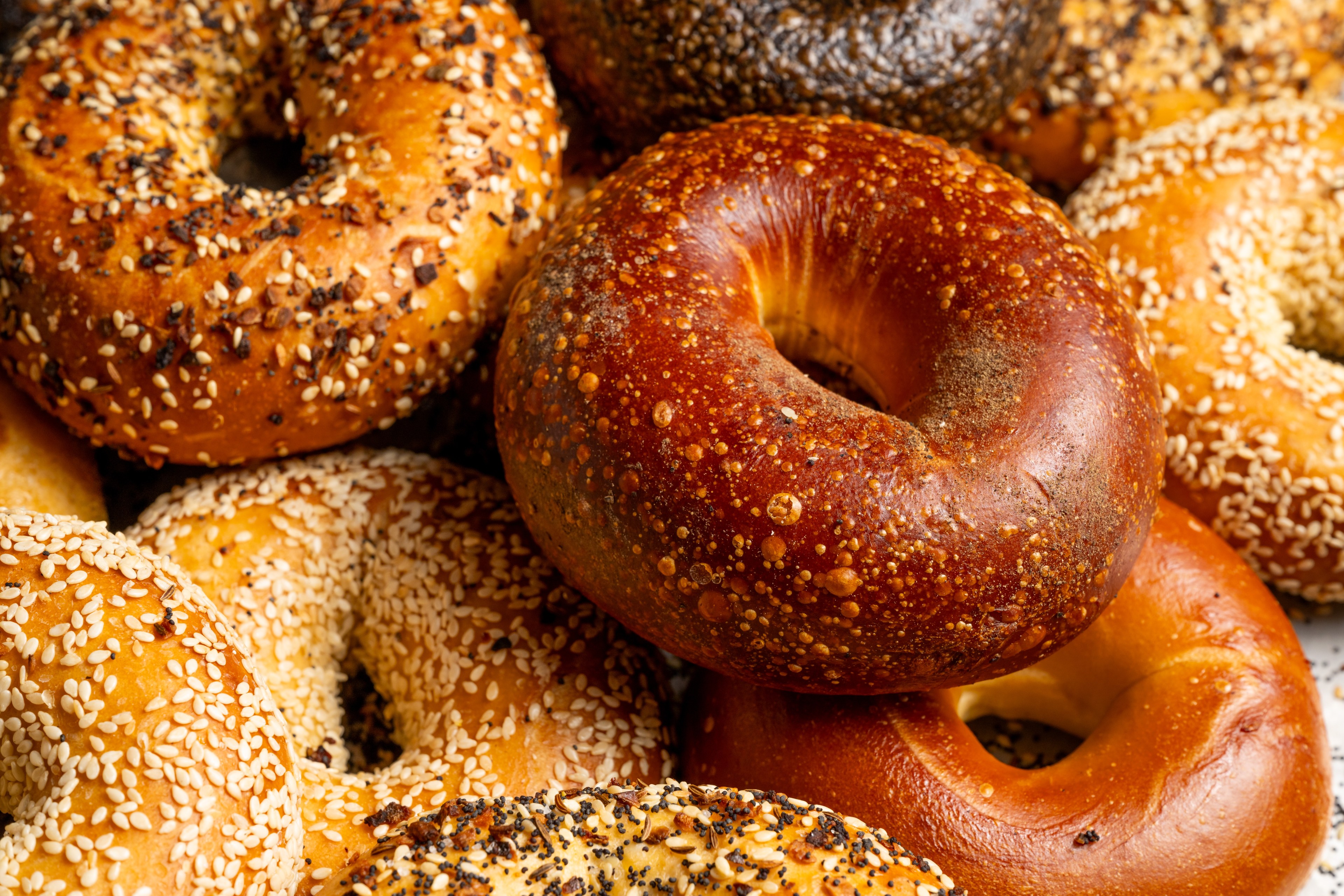 A close up of a pile of bagels of various flavor.