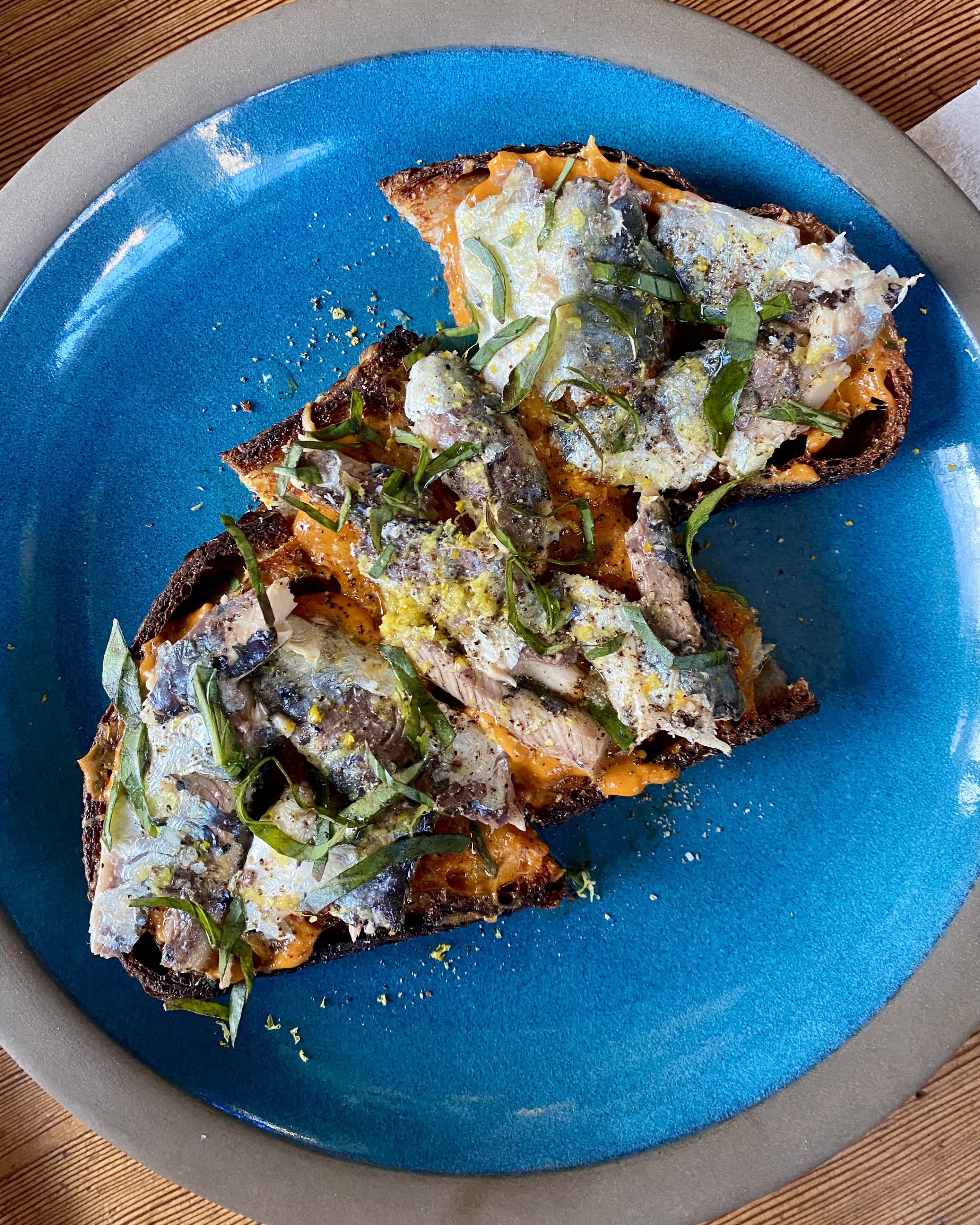 An open-faced sandwich topped with anchovies and fresh herbs on a plate ceramic plate.