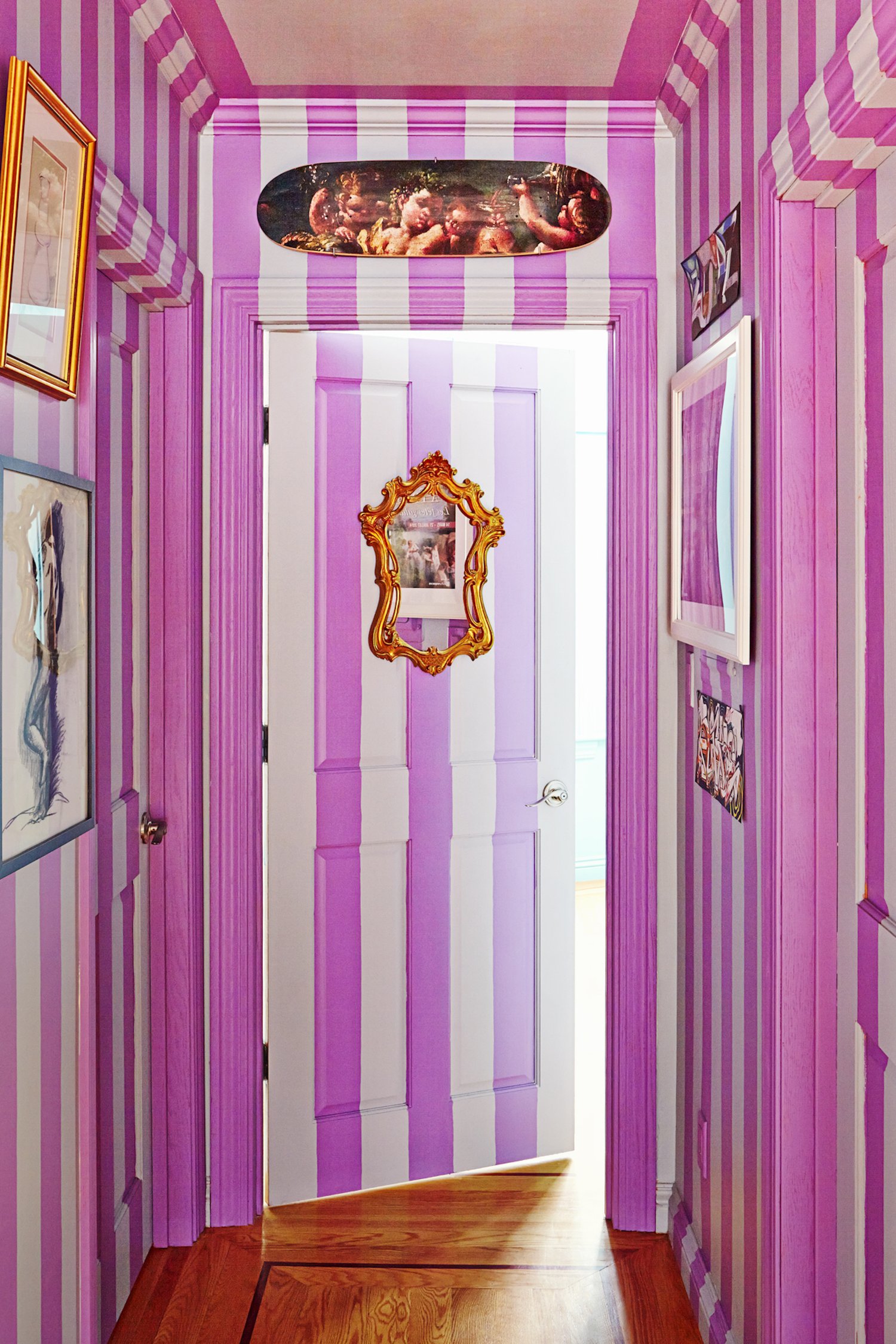 A hallway features magenta and white vertical striped walls and doors. The door has a gold ornate mirror, and framed artwork decorates the walls.