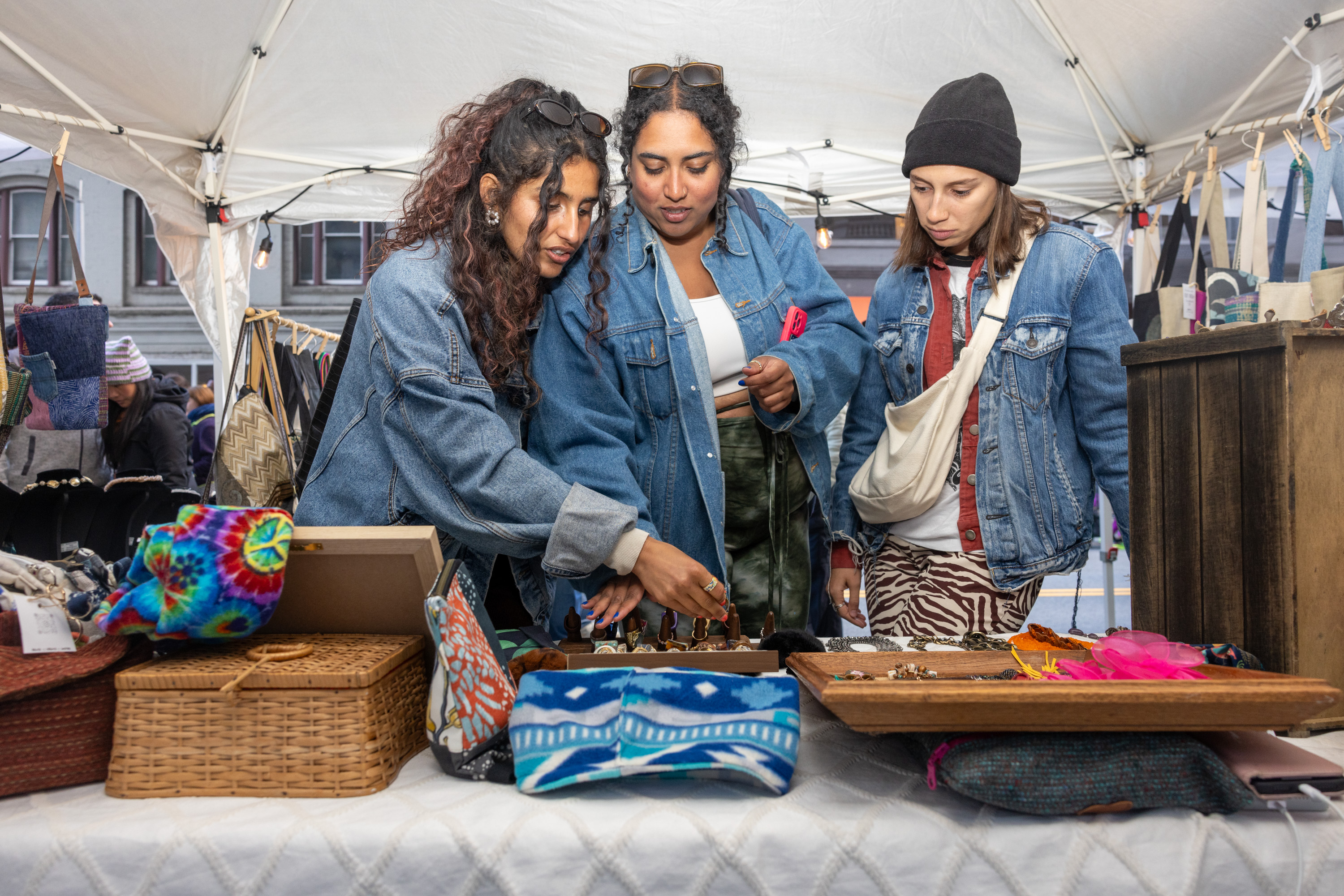 Three women look at jewelry at an artisan's booth. 