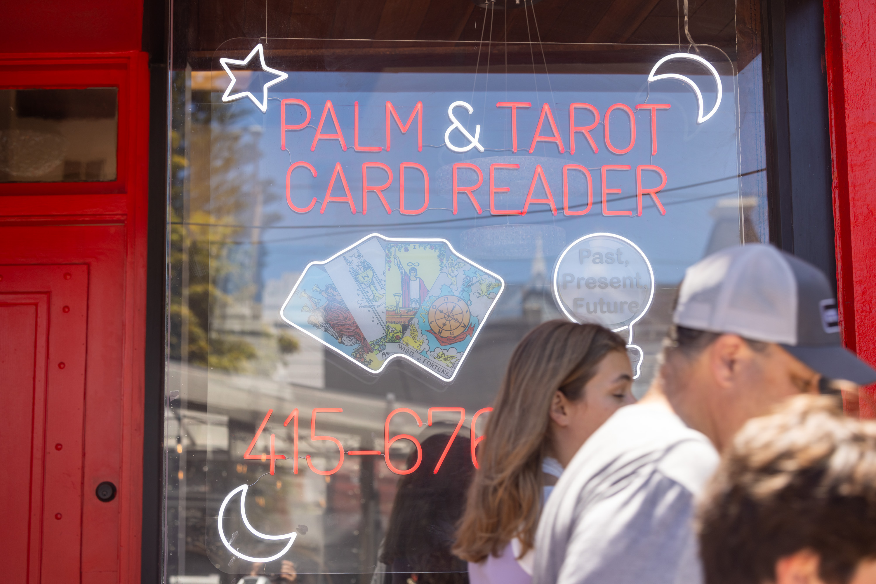 A neon sign advertises &quot;Palm &amp; Tarot Card Reader&quot; with tarot cards, a star, and a crescent moon. The text &quot;Past, Present, Future&quot; and a phone number are also visible.