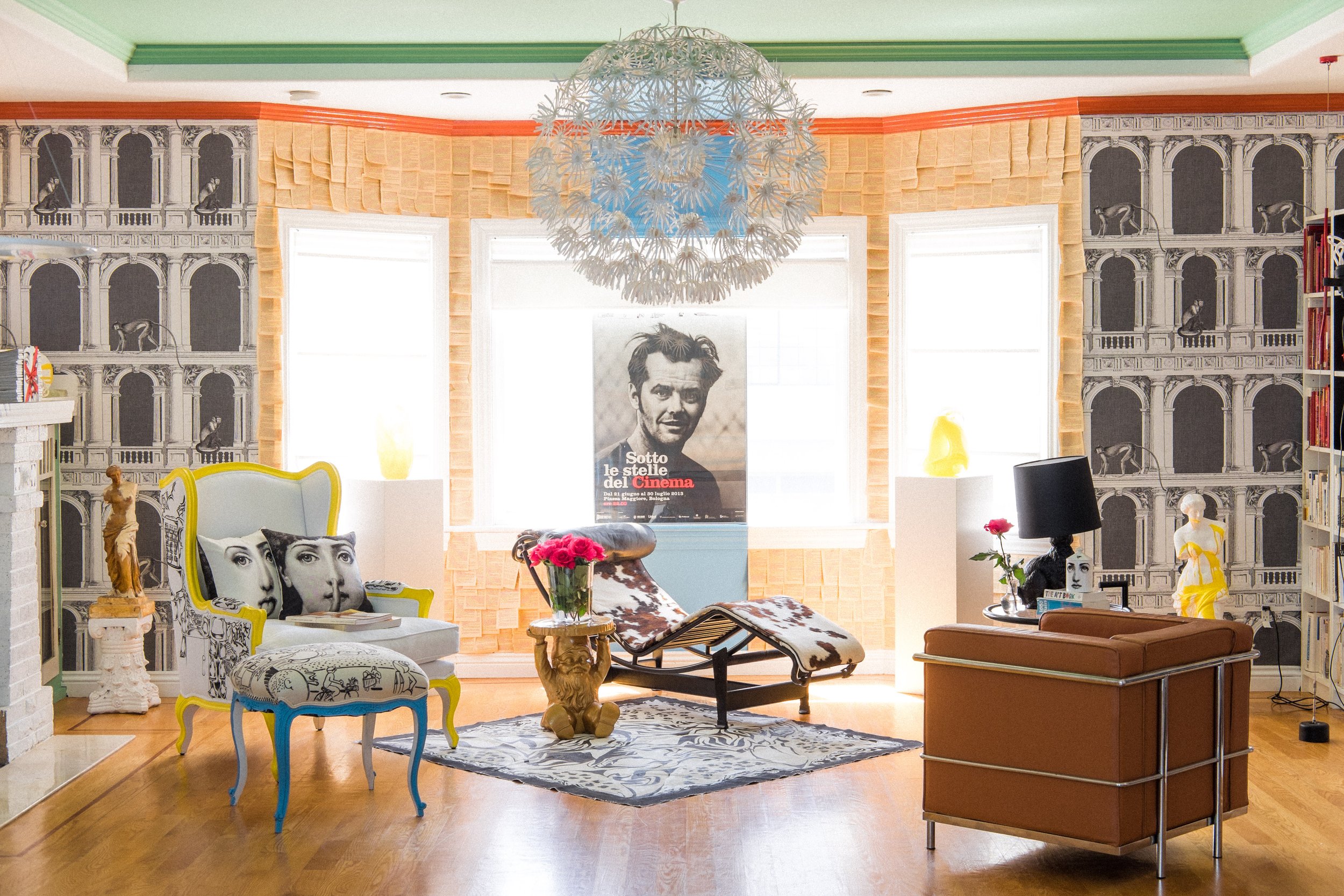 A vibrant room features eclectic furniture, bold wall art, a large dandelion-inspired chandelier, and a mix of classic and modern decor, including statues and patterned chairs.