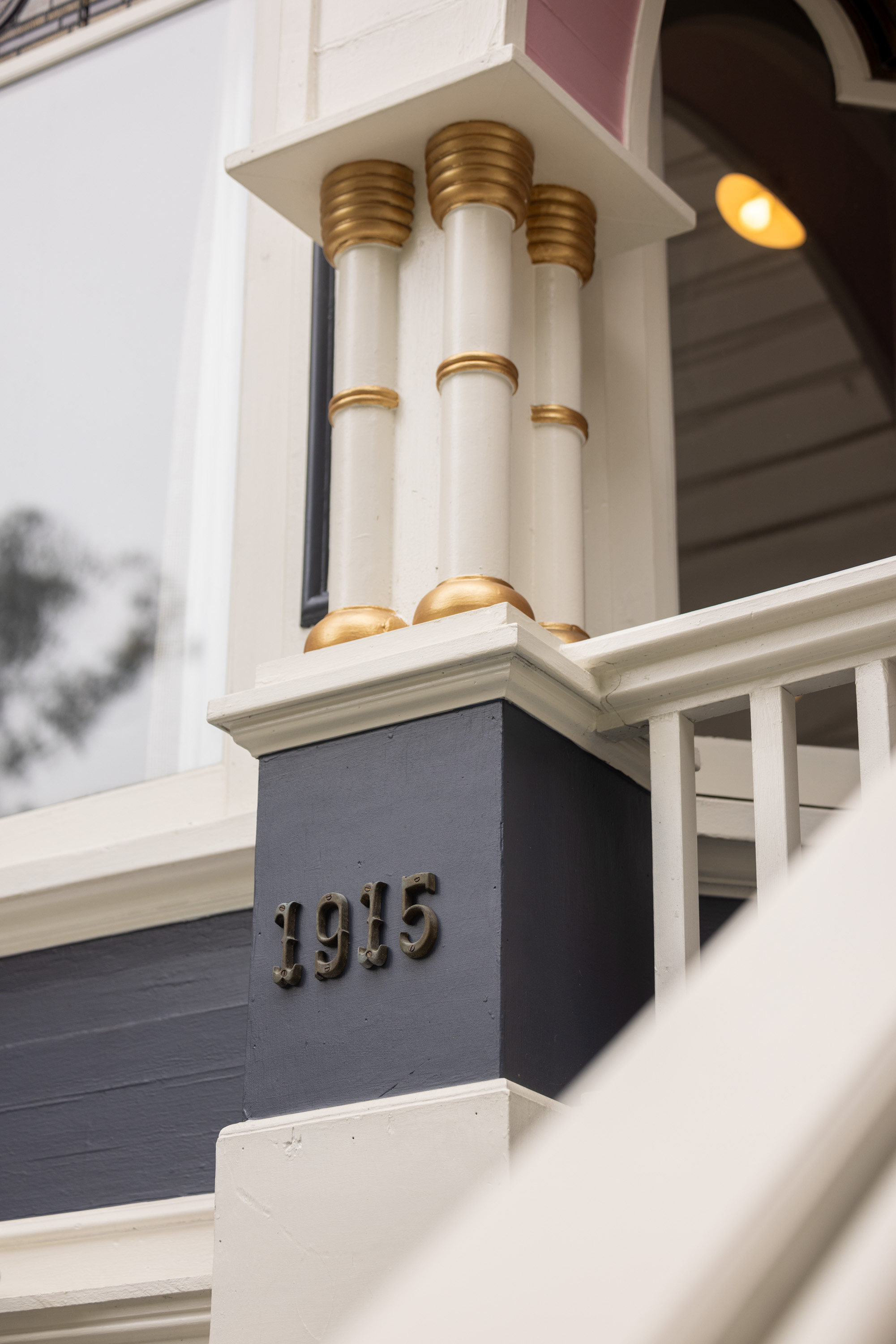 The image shows part of a building's exterior with ornate columns featuring gold accents and the number &quot;1915&quot; displayed on a dark blue panel.