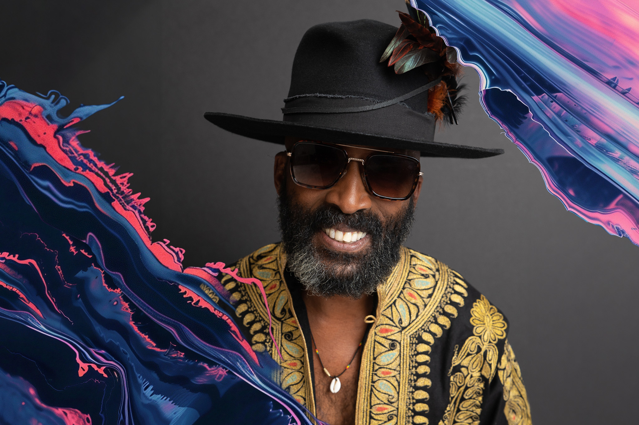 The musician D'Wayne Wiggins wears a black cowboy hat, sunglasses and gold shirt while smiling into the camera for a posed portrait.