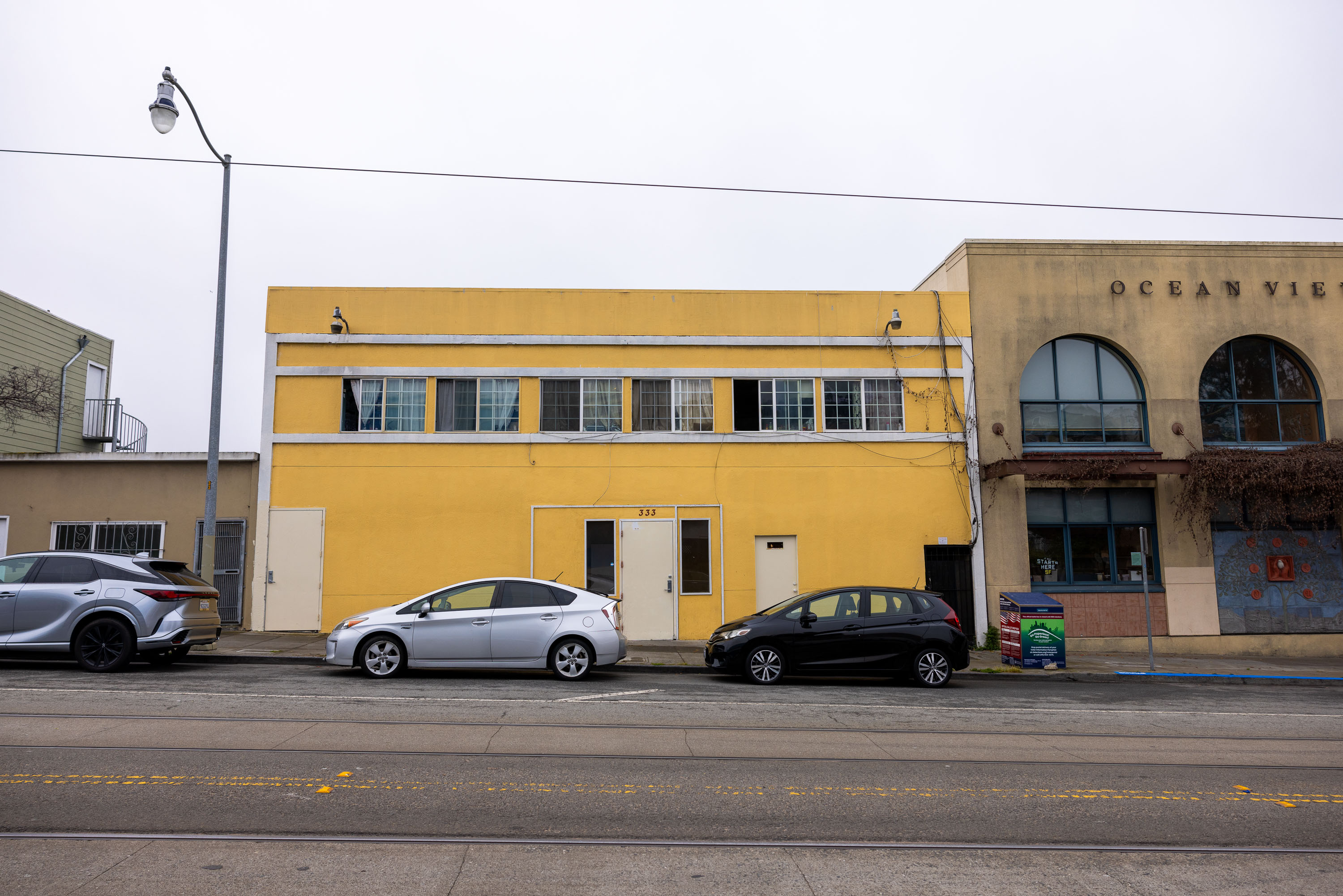 Three cars are parked in front of a yellow building with numerous windows. The building's street number is 333, and it has two doors visible from the street.