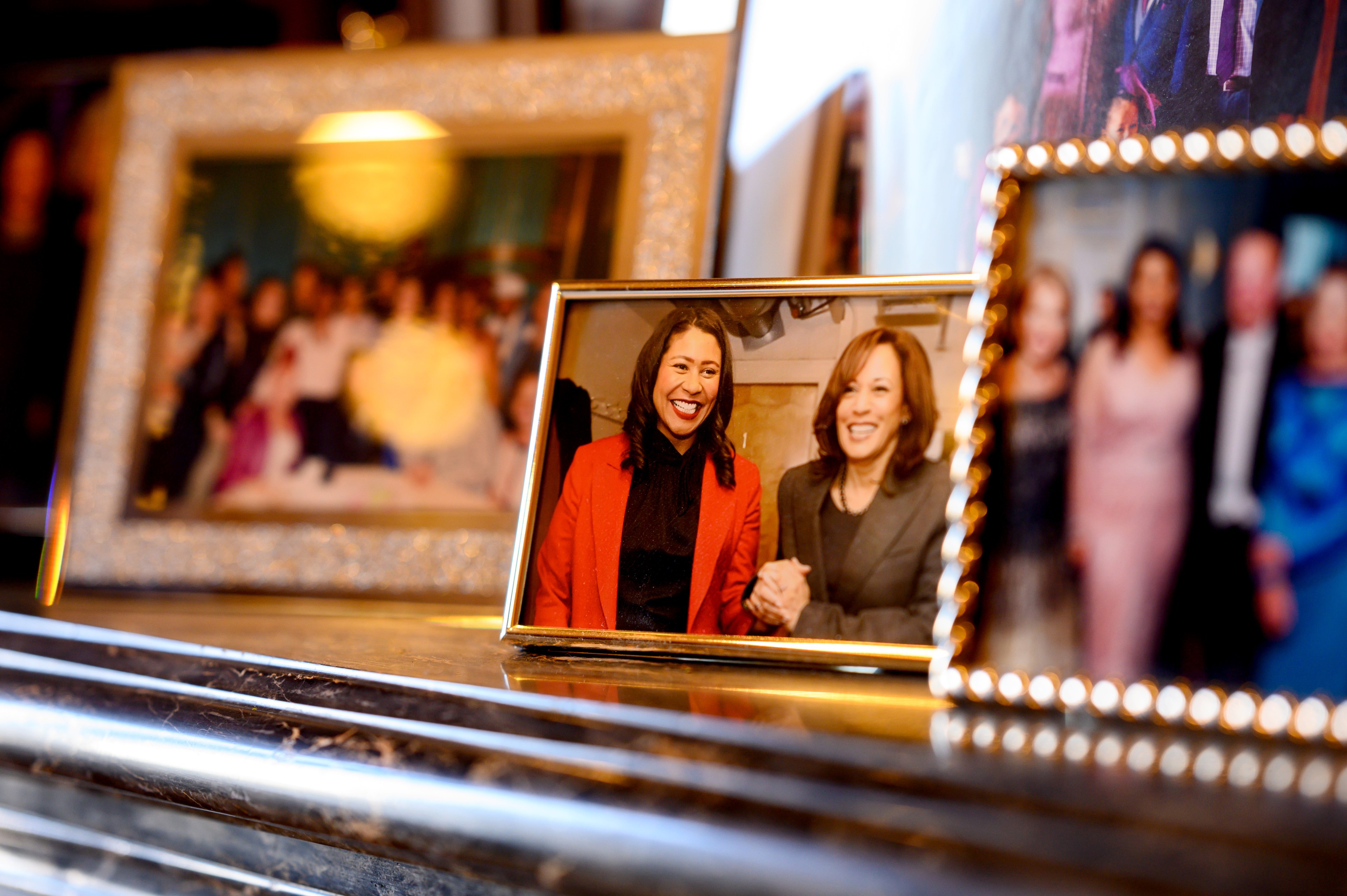 Multiple framed photos are displayed on a mantel, with the prominent one showing two smiling women holding hands. Other family and group photos surround it.