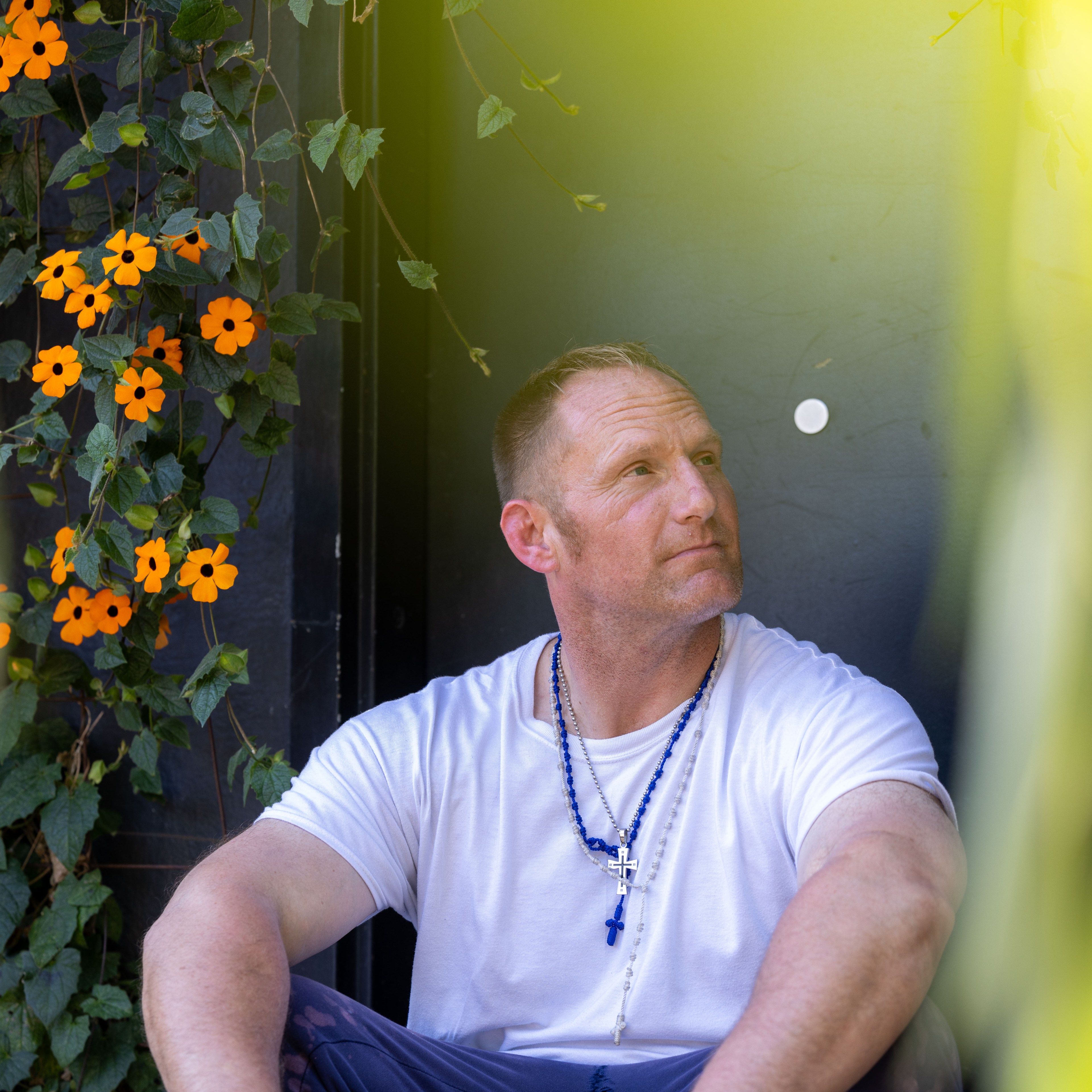 A man sits in a garden of flowers and greenery.