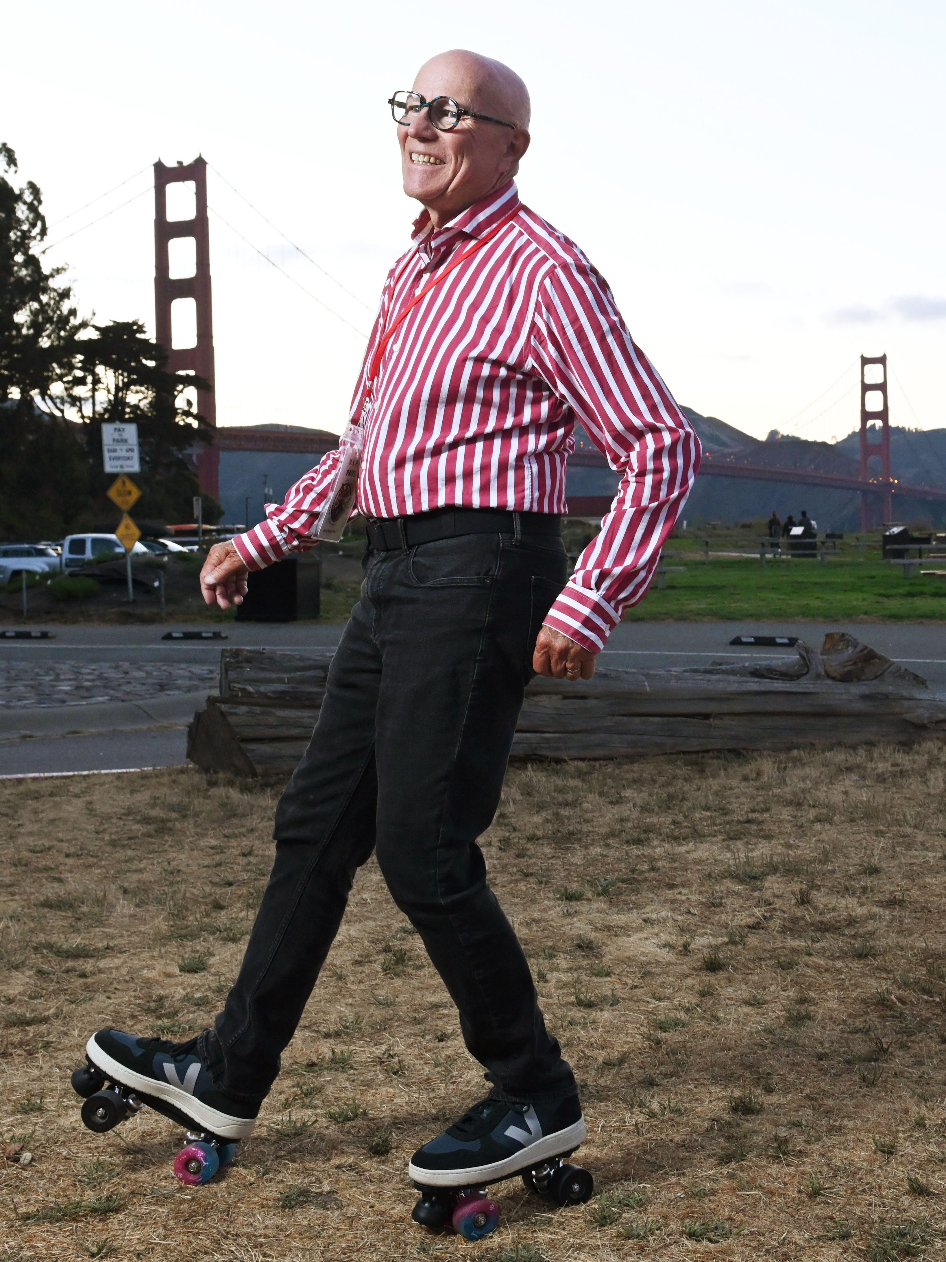 A person wearing a red and white striped shirt, black pants, and roller skates is smiling and skating on grass with the Golden Gate Bridge in the background.