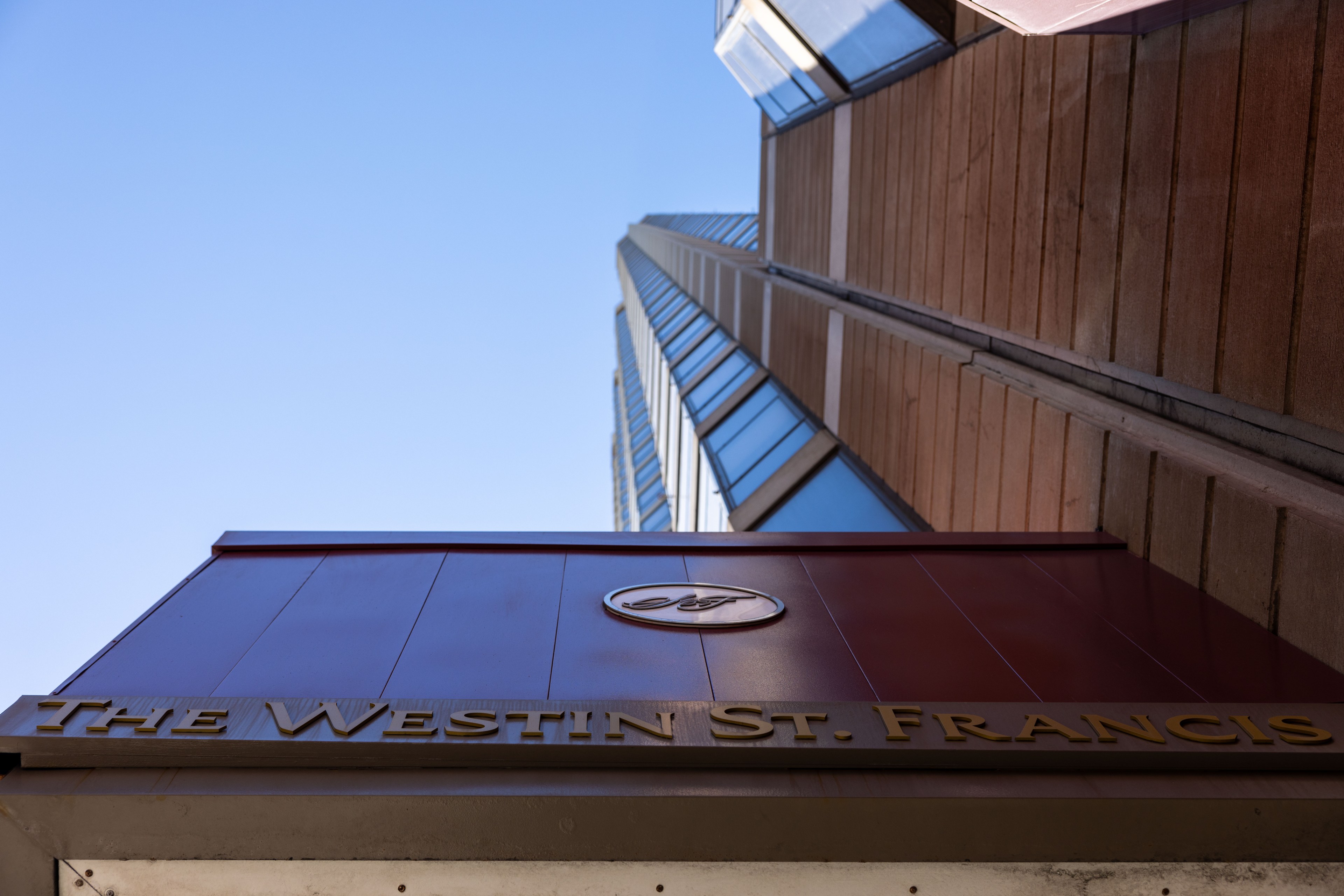 The image shows a tall building from a low angle, featuring a red awning with the words &quot;The Westin St. Francis&quot; in gold letters, set against a clear, blue sky.