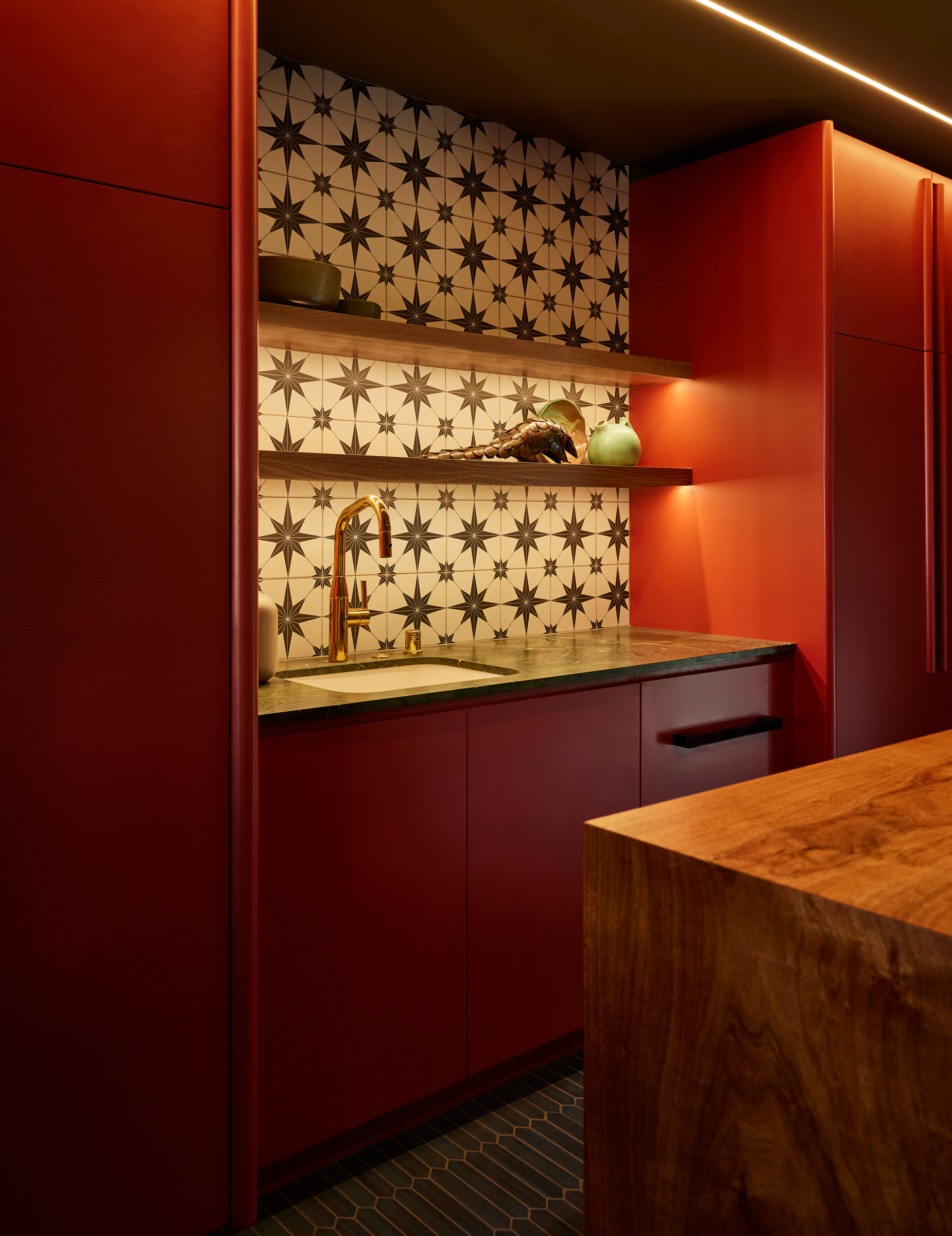 A modern kitchen features bold red cabinets, a brass faucet over a sink, and a black-and-white star-patterned tile backsplash with wood shelves displaying decorative items.