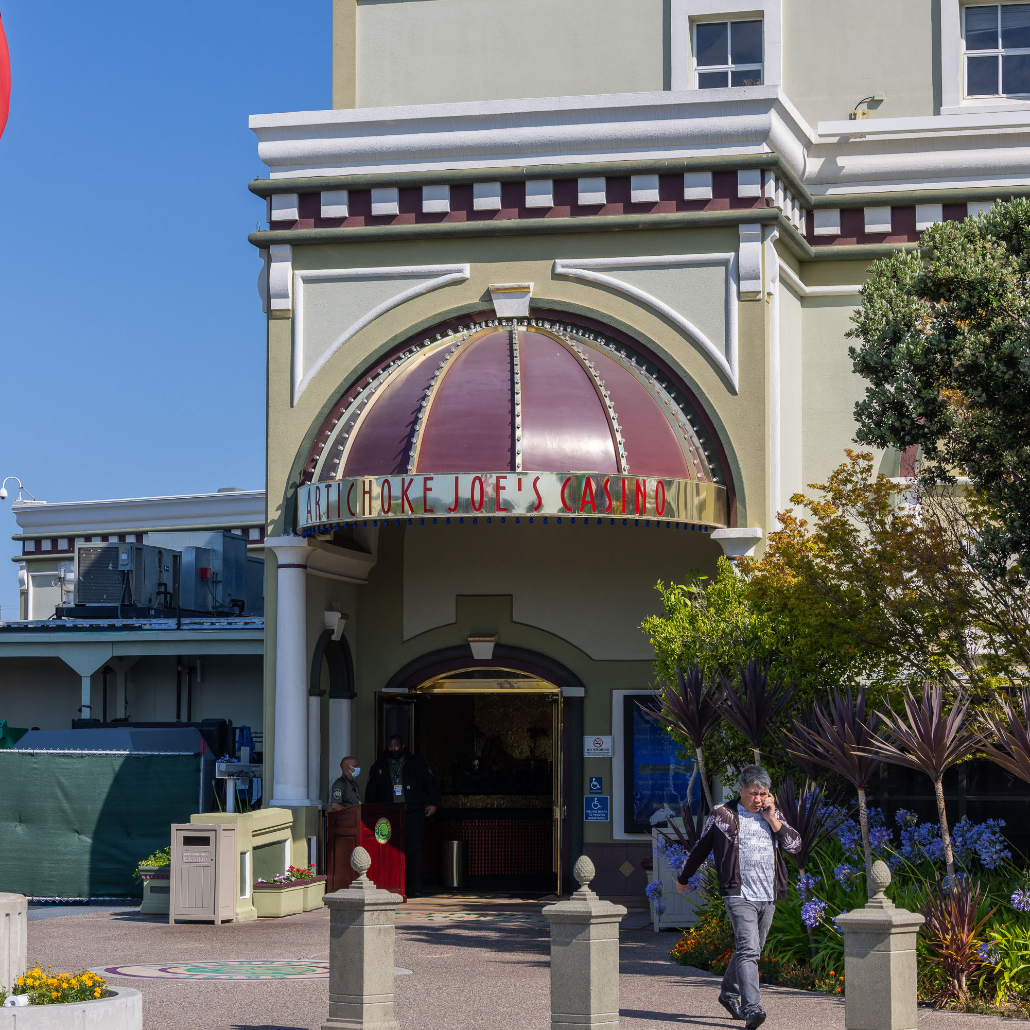 The image shows the entrance of Artichoke Joe's Casino, with an arched canopy above and a man walking while talking on the phone outside.