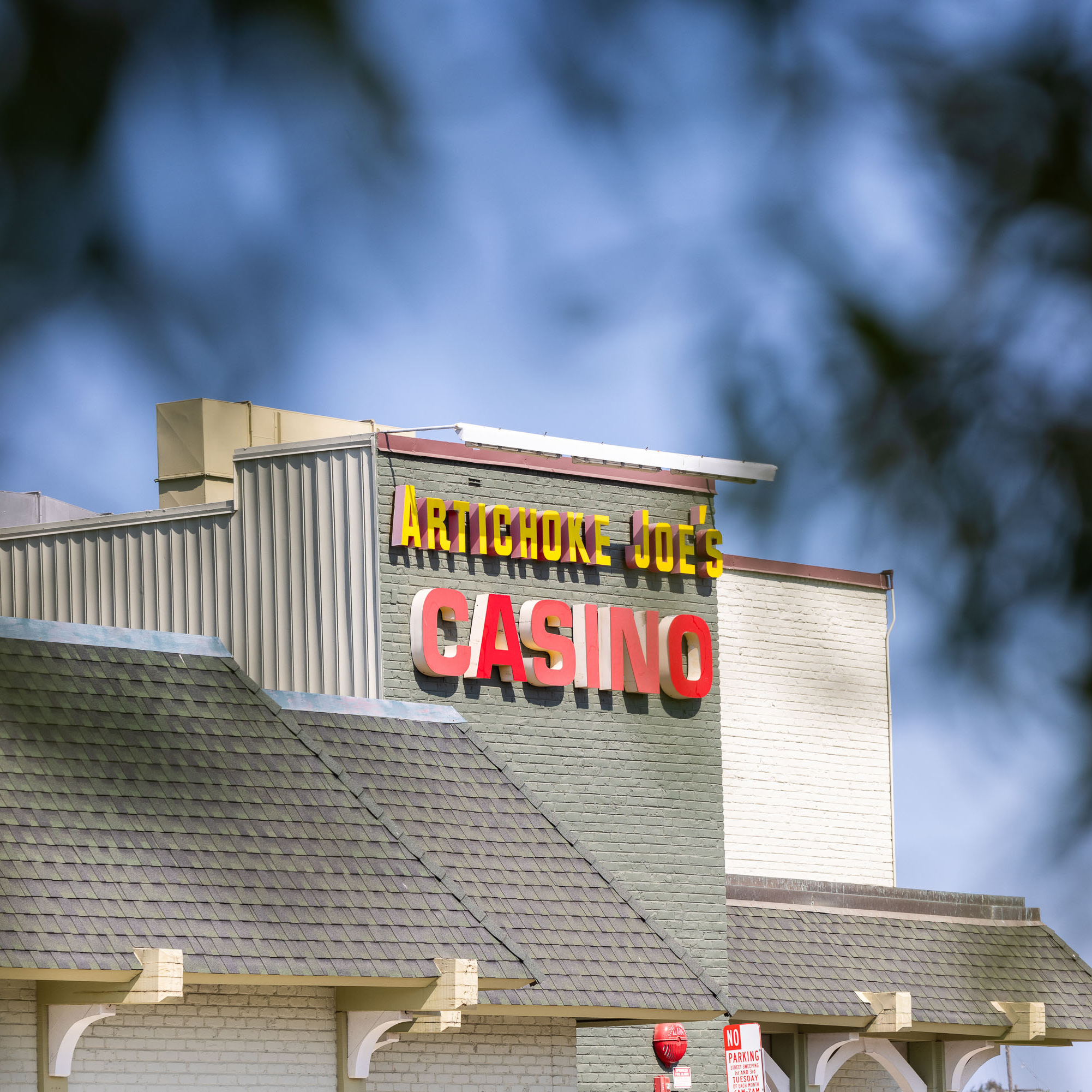 The image shows the facade of a building with a sign reading &quot;Artichoke Joe's Casino&quot; in large red and yellow letters, set against a clear, blue sky.