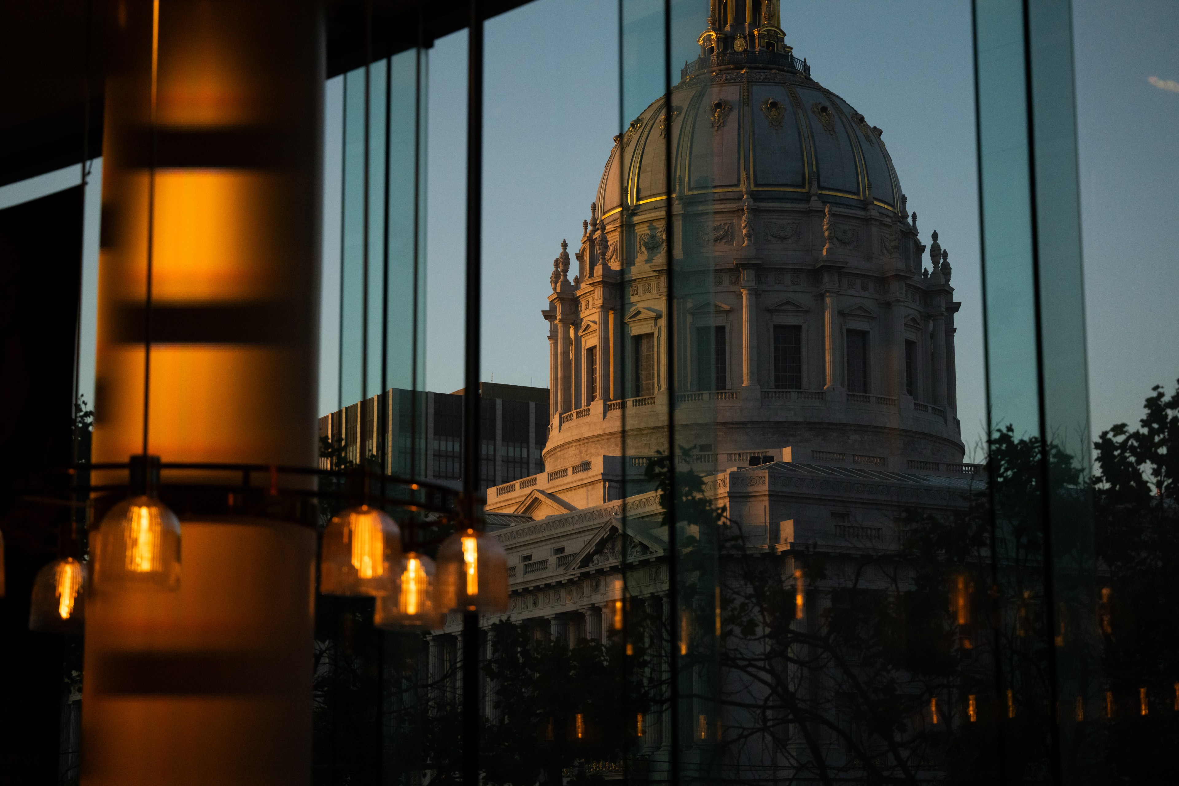 The image shows a majestic domed building viewed through glass panels, with warm interior lighting and reflections creating a serene, golden ambiance.