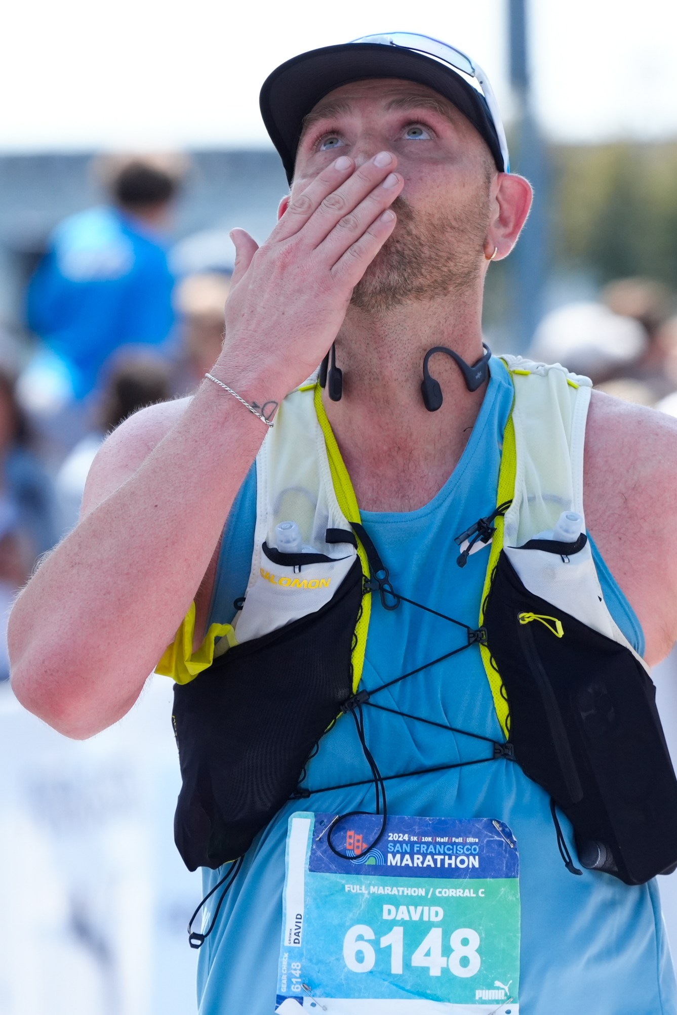 A man wearing a vest and tank top holds his hand over his face as he looks overhead.