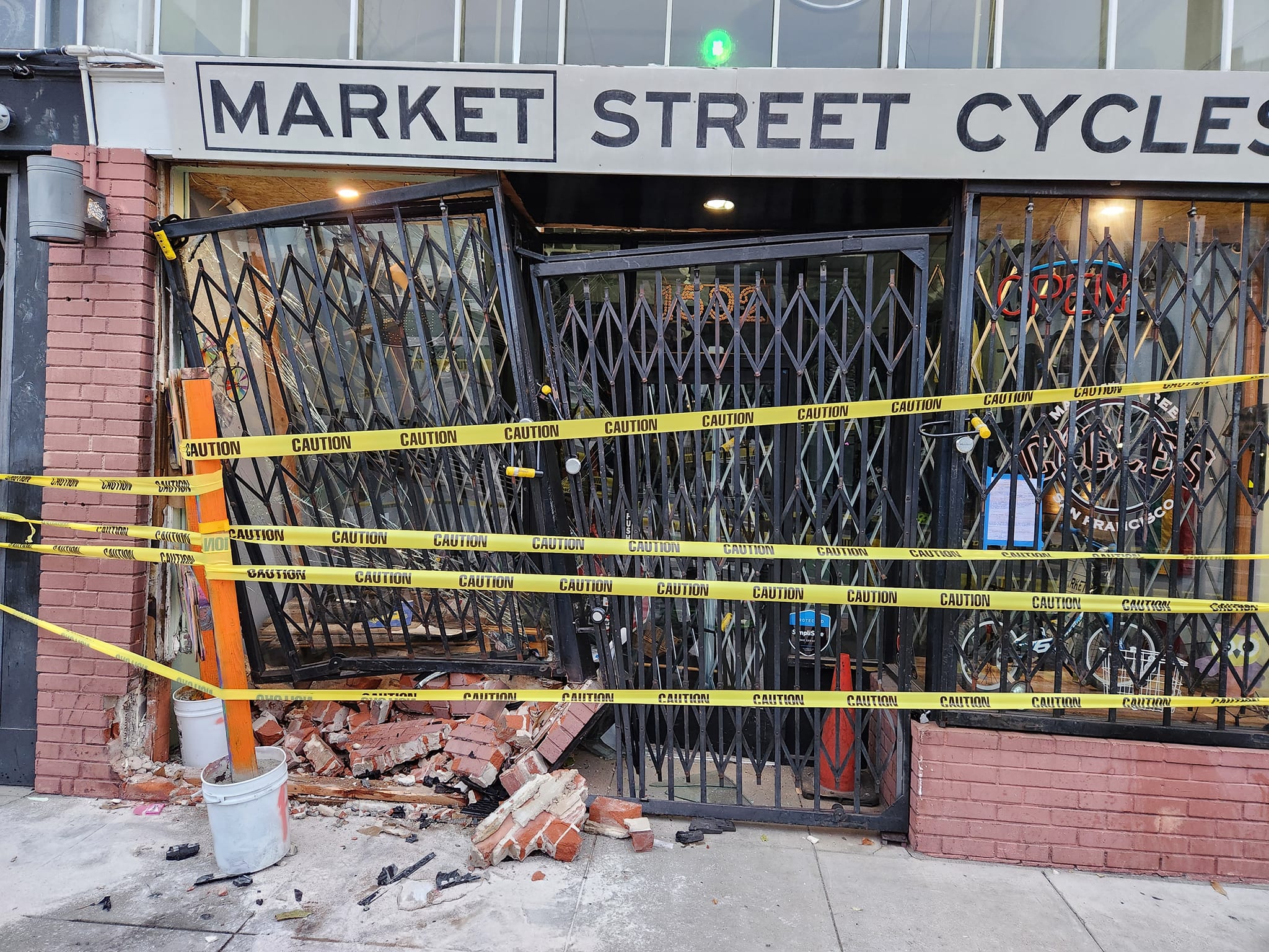 A storefront of a metal-gated bicycle shop is covered by caution tape