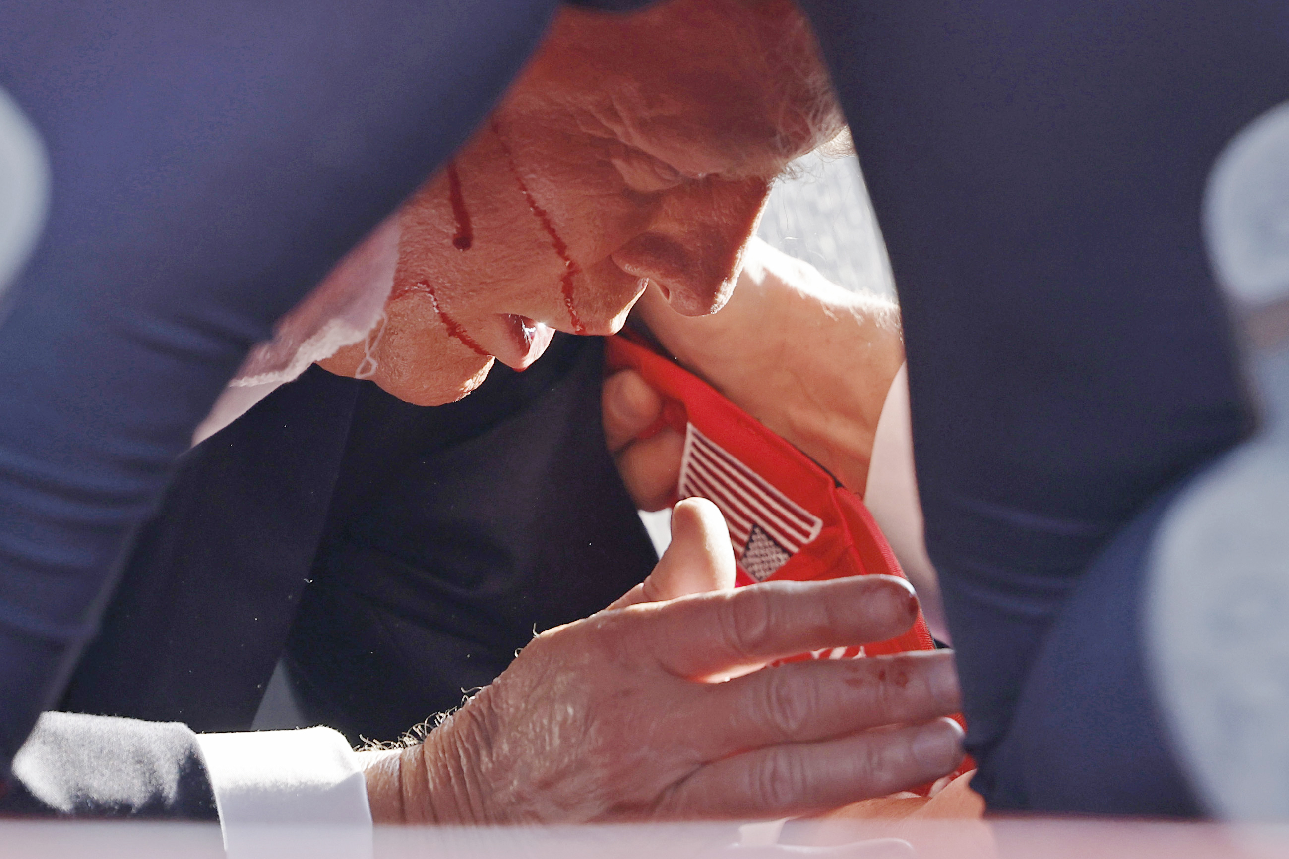 A person is leaning forward with blood streaming from their forehead. The individual appears to be in distress, tightly holding a red piece of fabric.