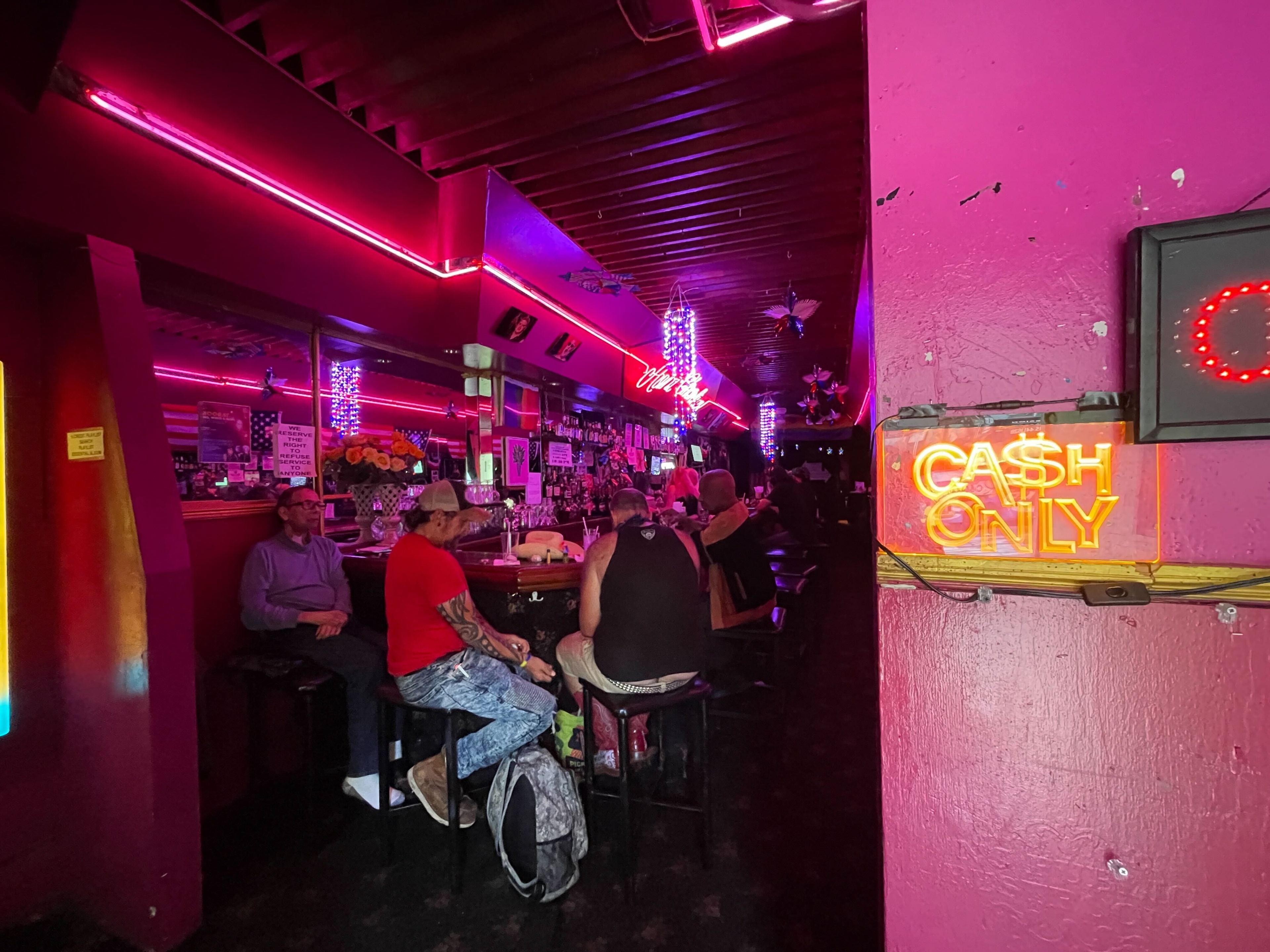 Peeking through the door of a brightly colored bar, with a &quot;cash only&quot; sign outside the entrance.