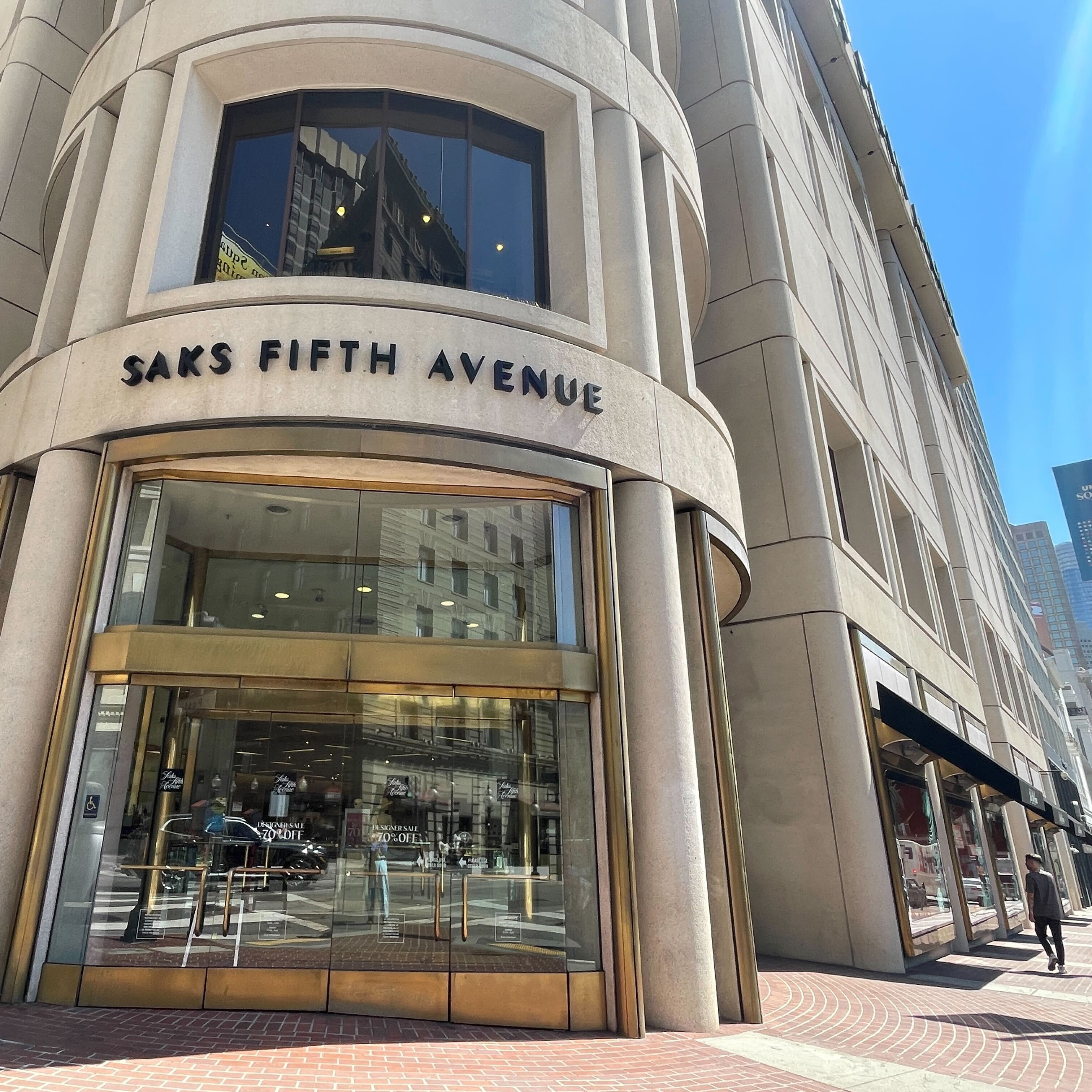 A person walks by on the right of the entrance of a big store, with the words Saks Fifth Avenue on the building