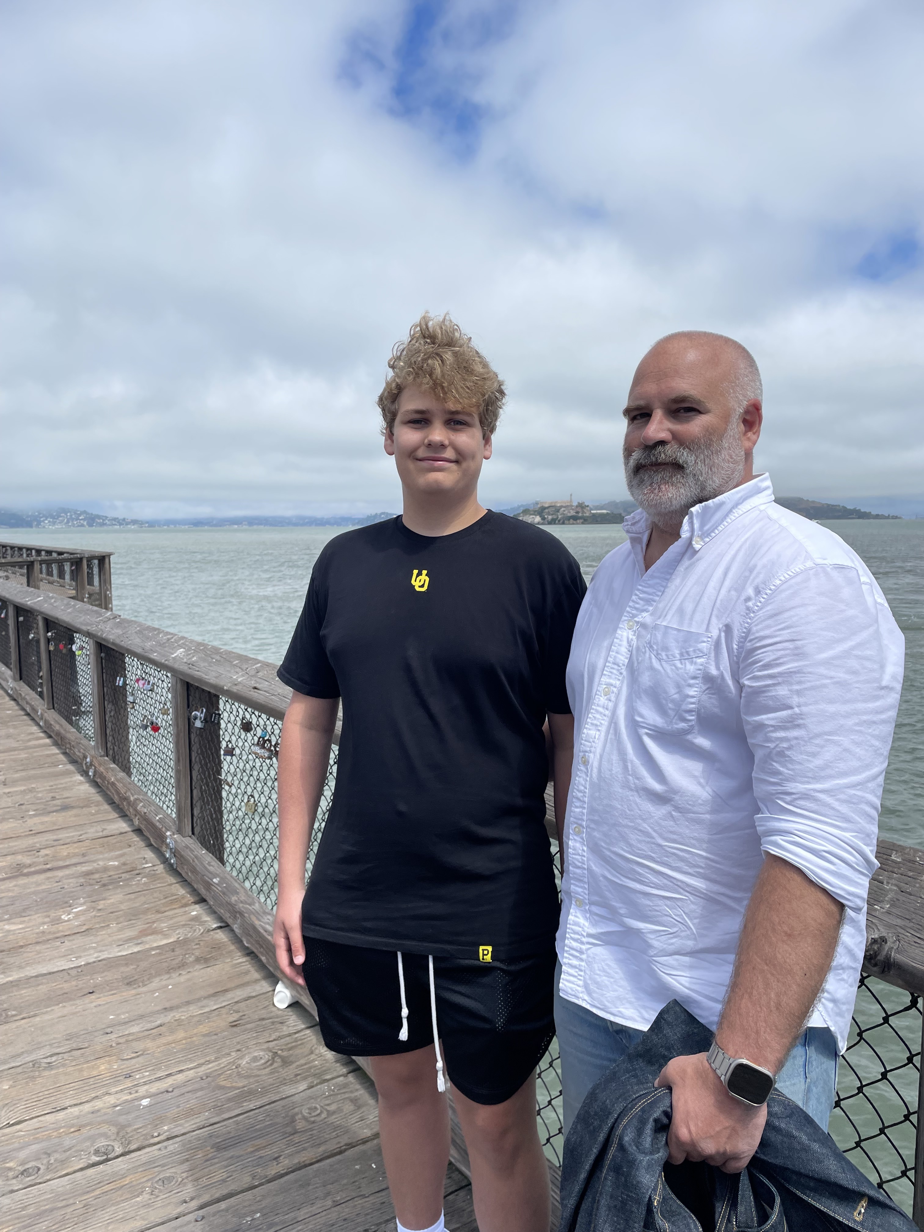 A teenage boy and a middle-aged man pose next to each other on a dock for a photo.