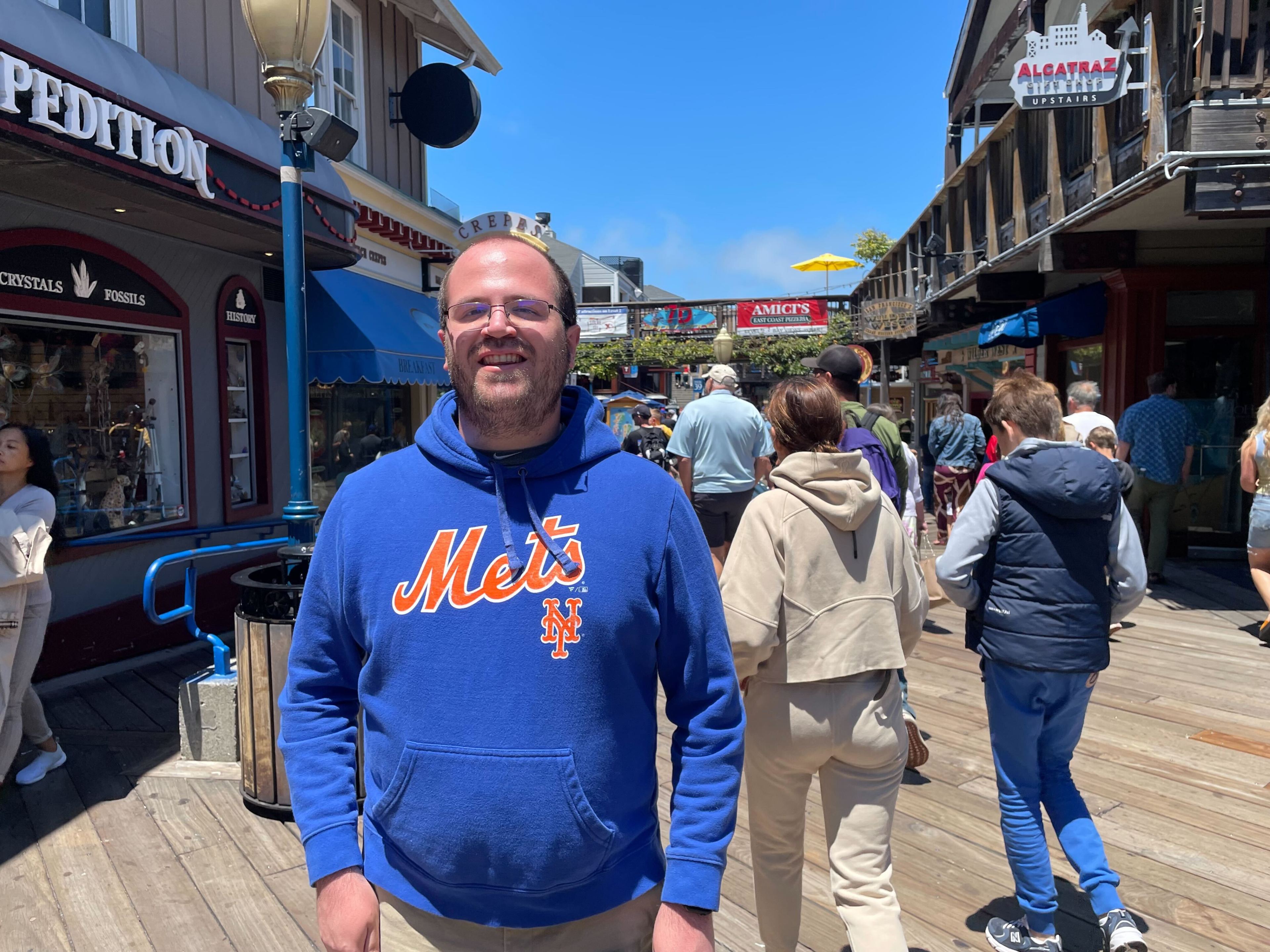 A man wearing blue sweatshirt stands for a photo on a pier.