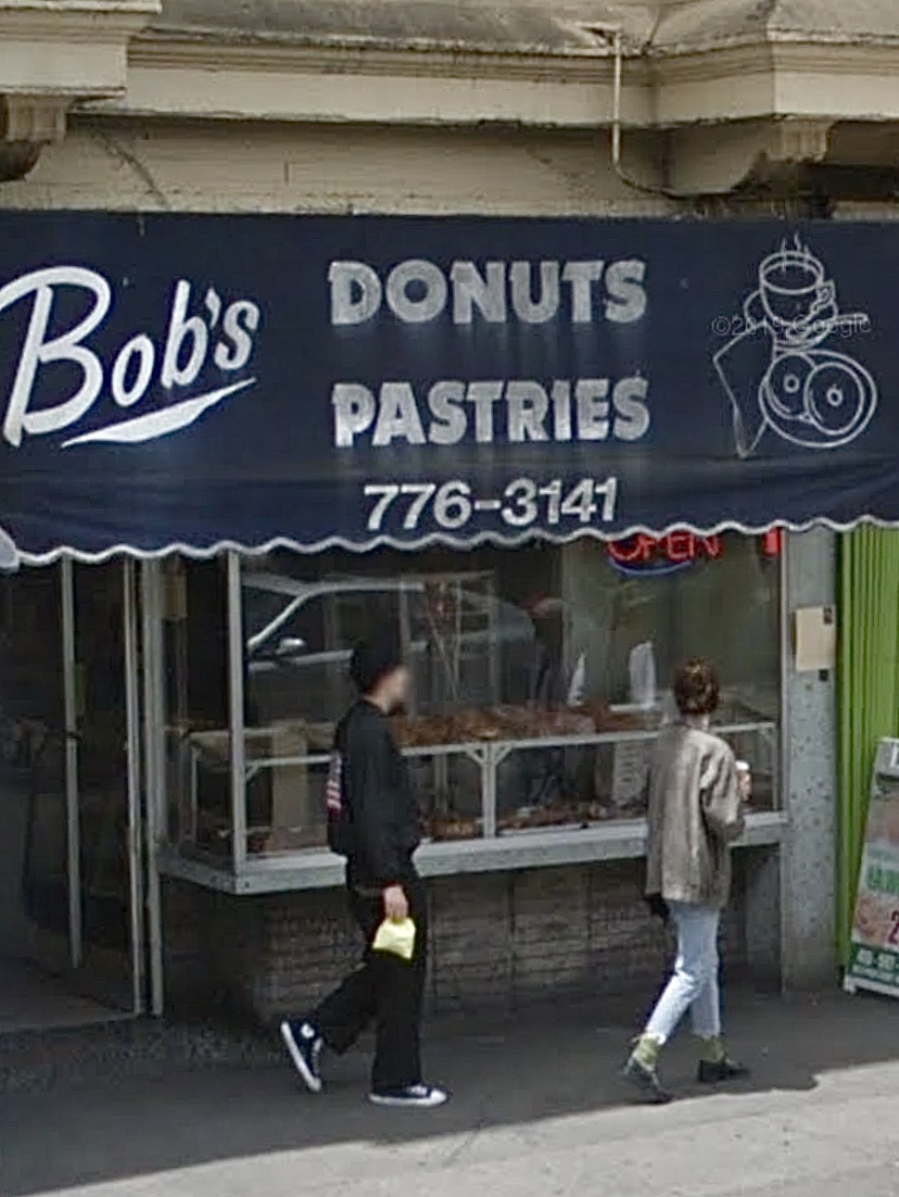 The image shows a storefront with a blue awning that reads &quot;Bob's Donuts Pastries&quot; along with a phone number, 776-3141. Two people are walking past the shop.