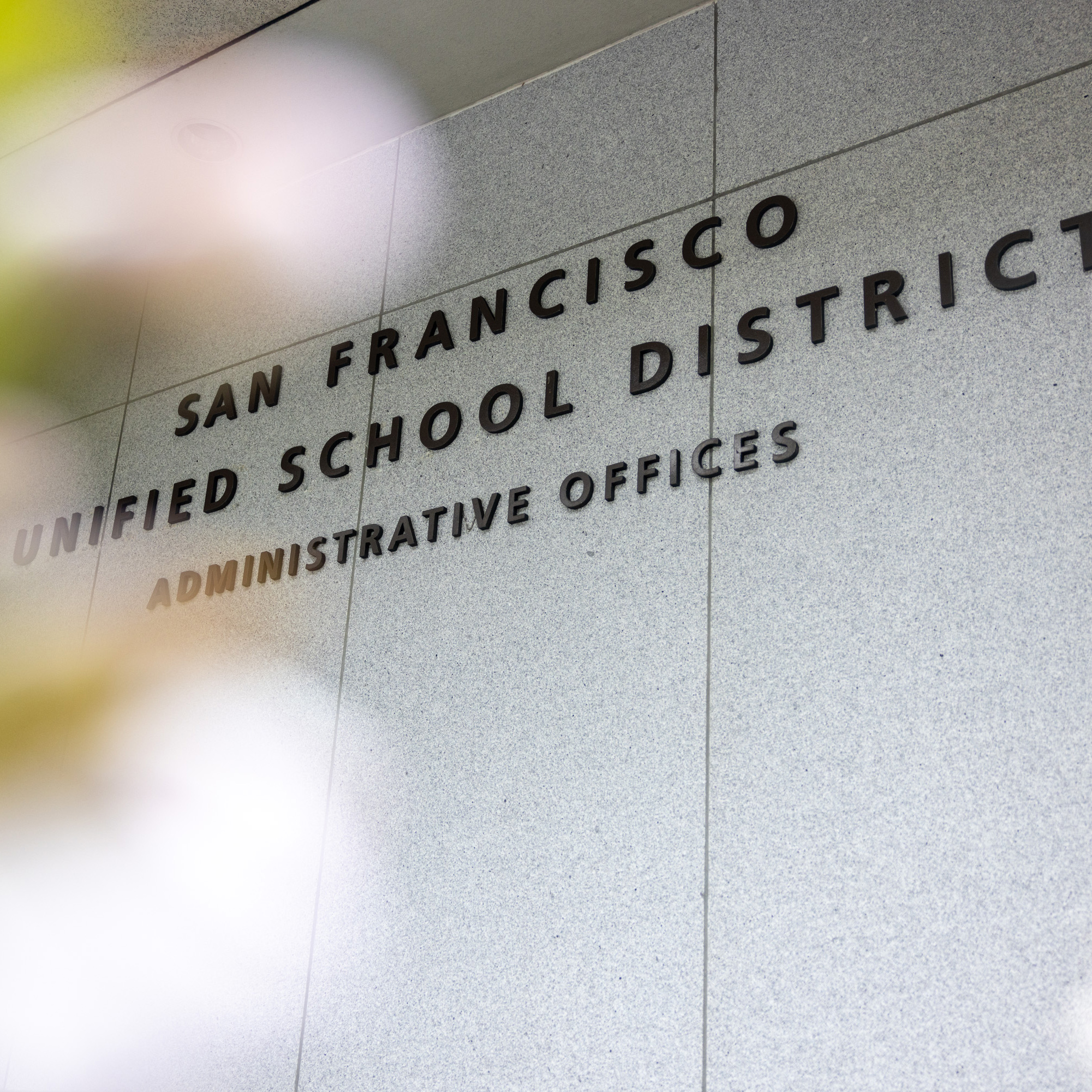 The image shows the entrance wall of a building with the text &quot;San Francisco Unified School District Administrative Offices&quot; in black capital letters.