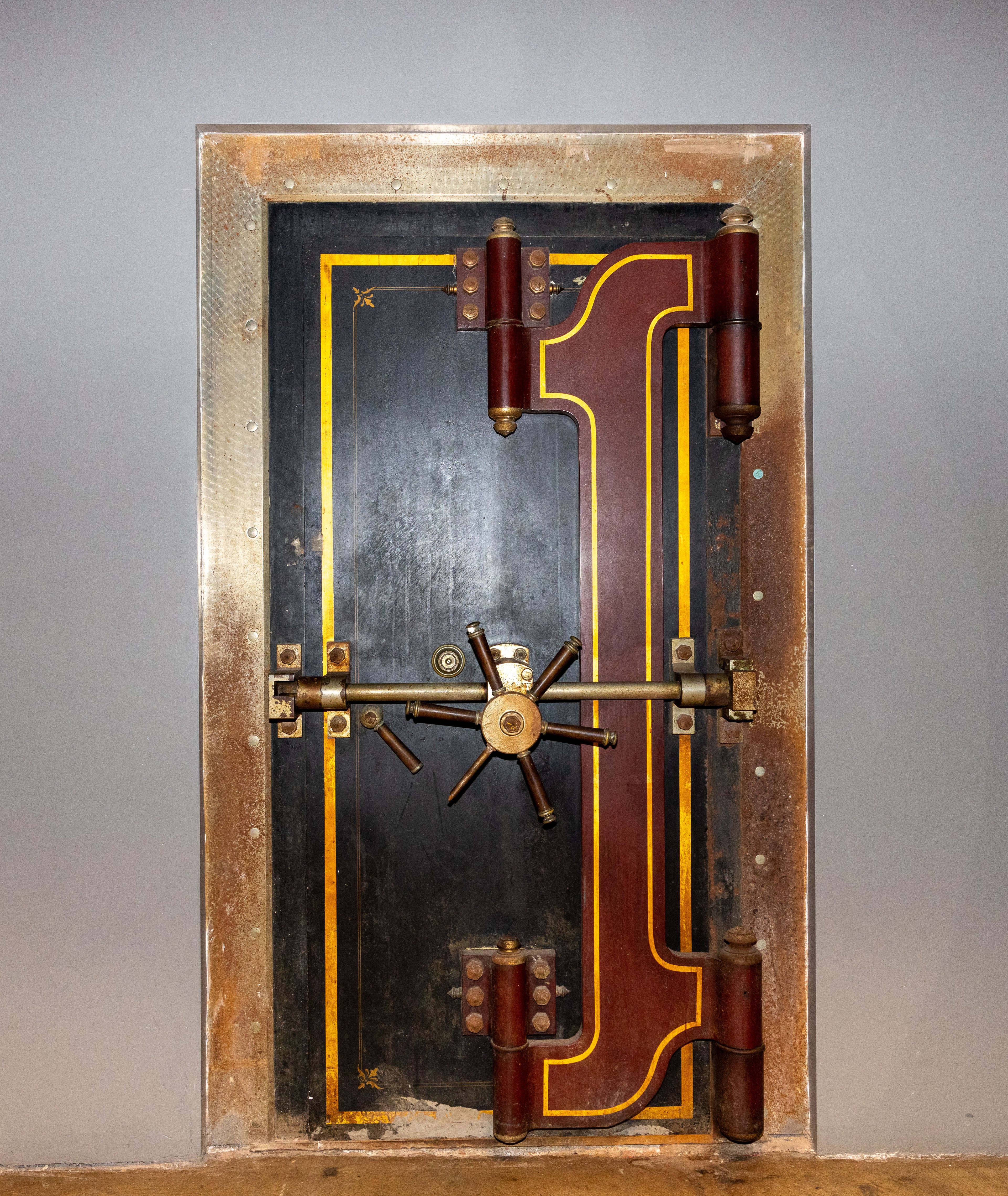 The image shows a vintage bank vault door with brass detailing, a large central lock wheel, and decorative yellow and red lines on a black background.