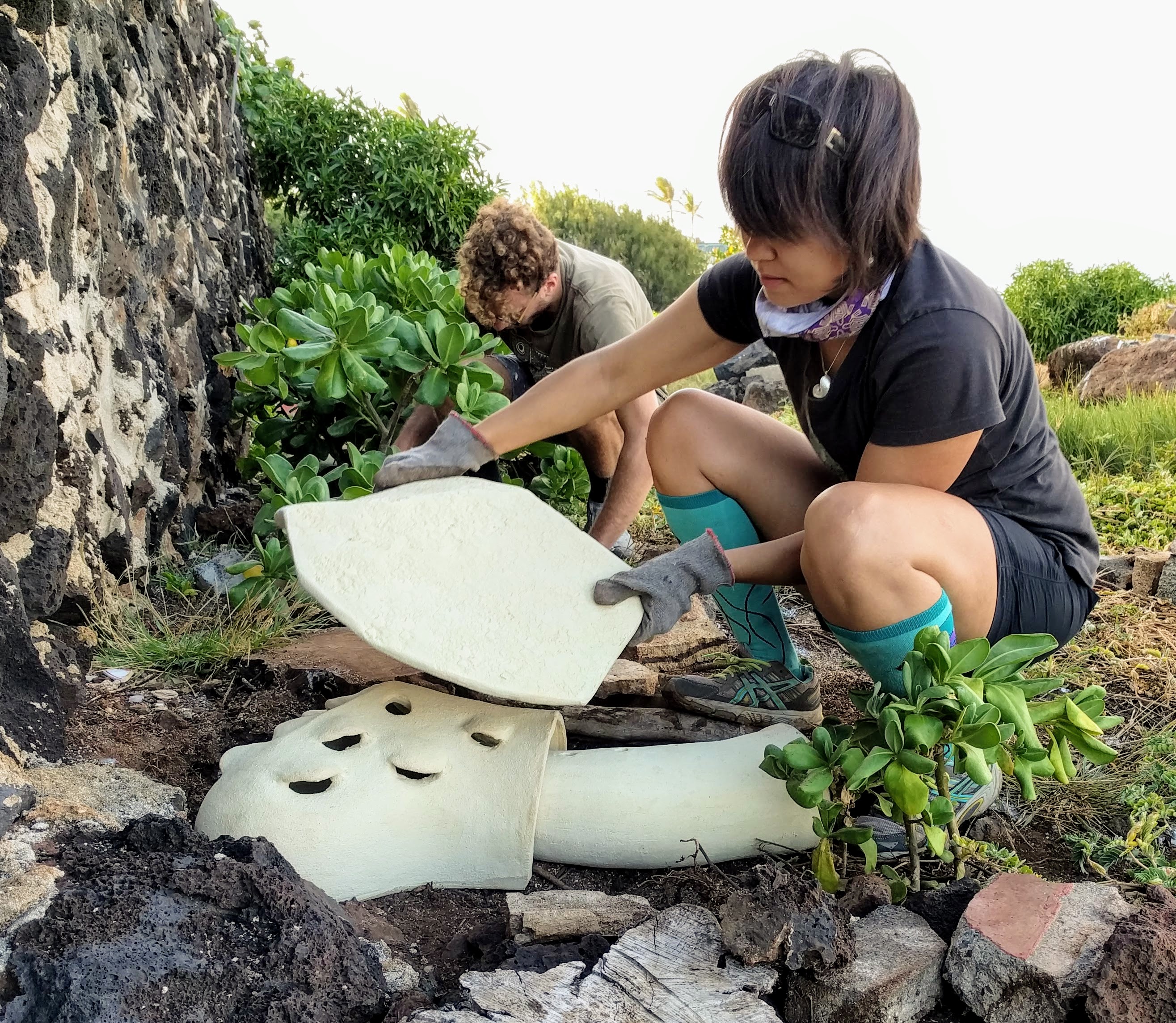 A person in green socks places a heat shield over a ceramic nest. 