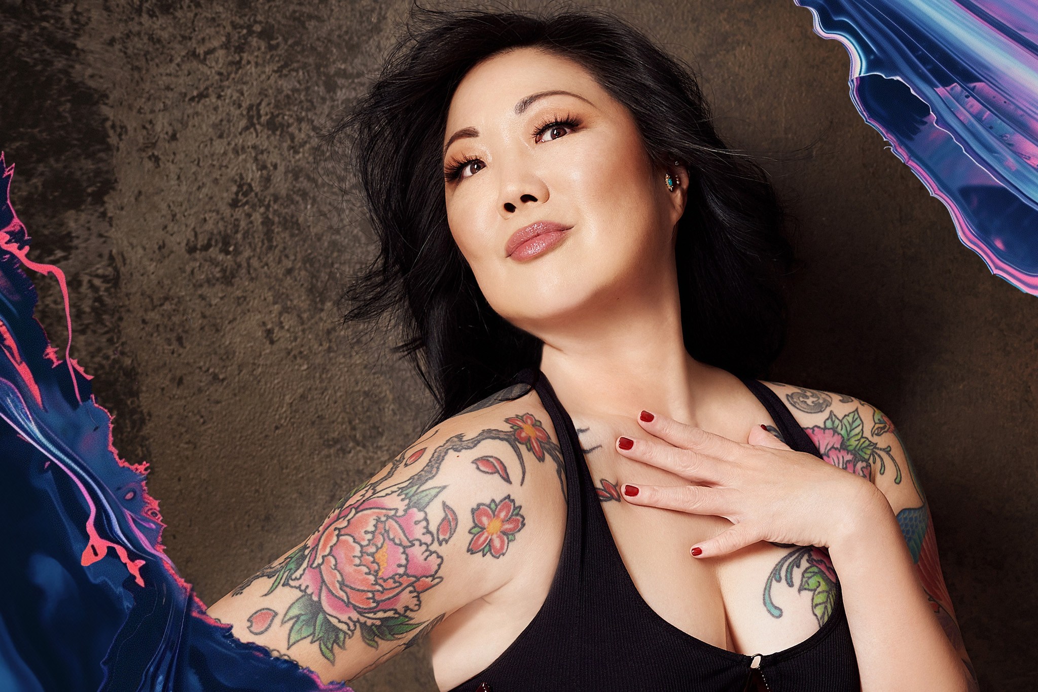 Margaret Cho poses in a black tank top, showing off the color tattoos on her arms.