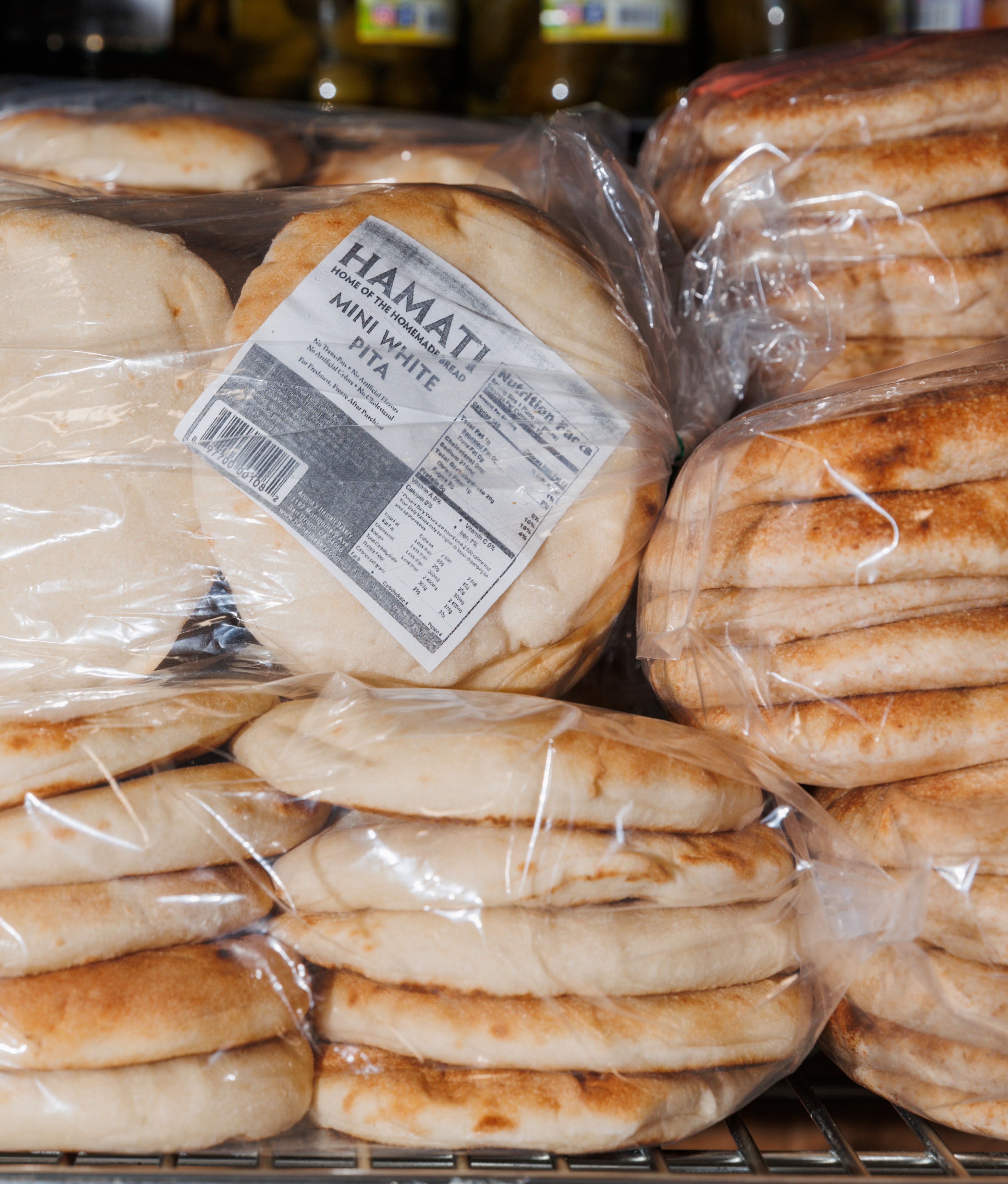 The image shows several packages of mini white pita bread, labeled with nutritional information, stacked on a metal shelf in a store.