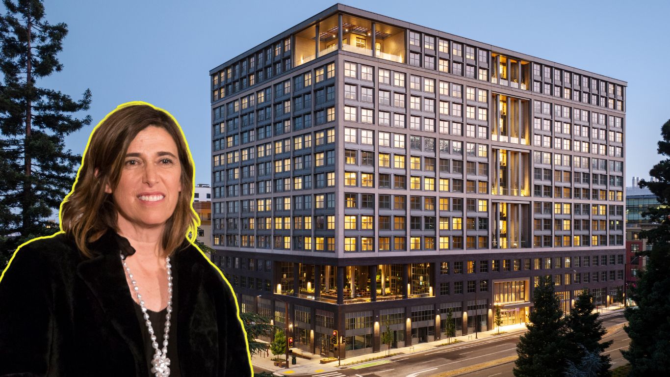 A woman with shoulder-length brown hair wearing a black jacket appears in front of a lit-up, modern, multi-story building during twilight. Trees frame the scene.