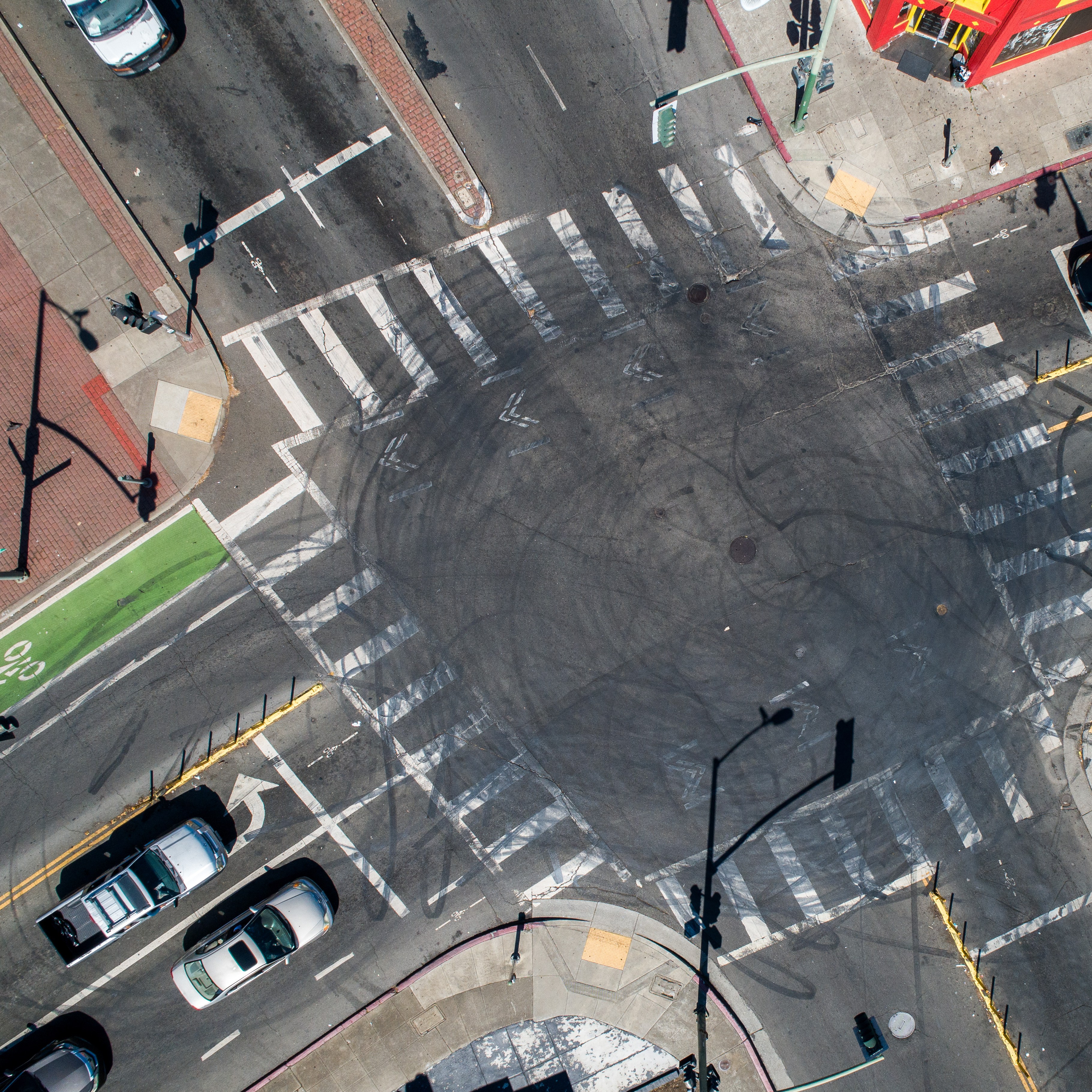 Aerial view of a busy intersection with multiple crosswalks, bike lanes, cars at stoplights, and a red building at the top. Skid marks are visible in the center.