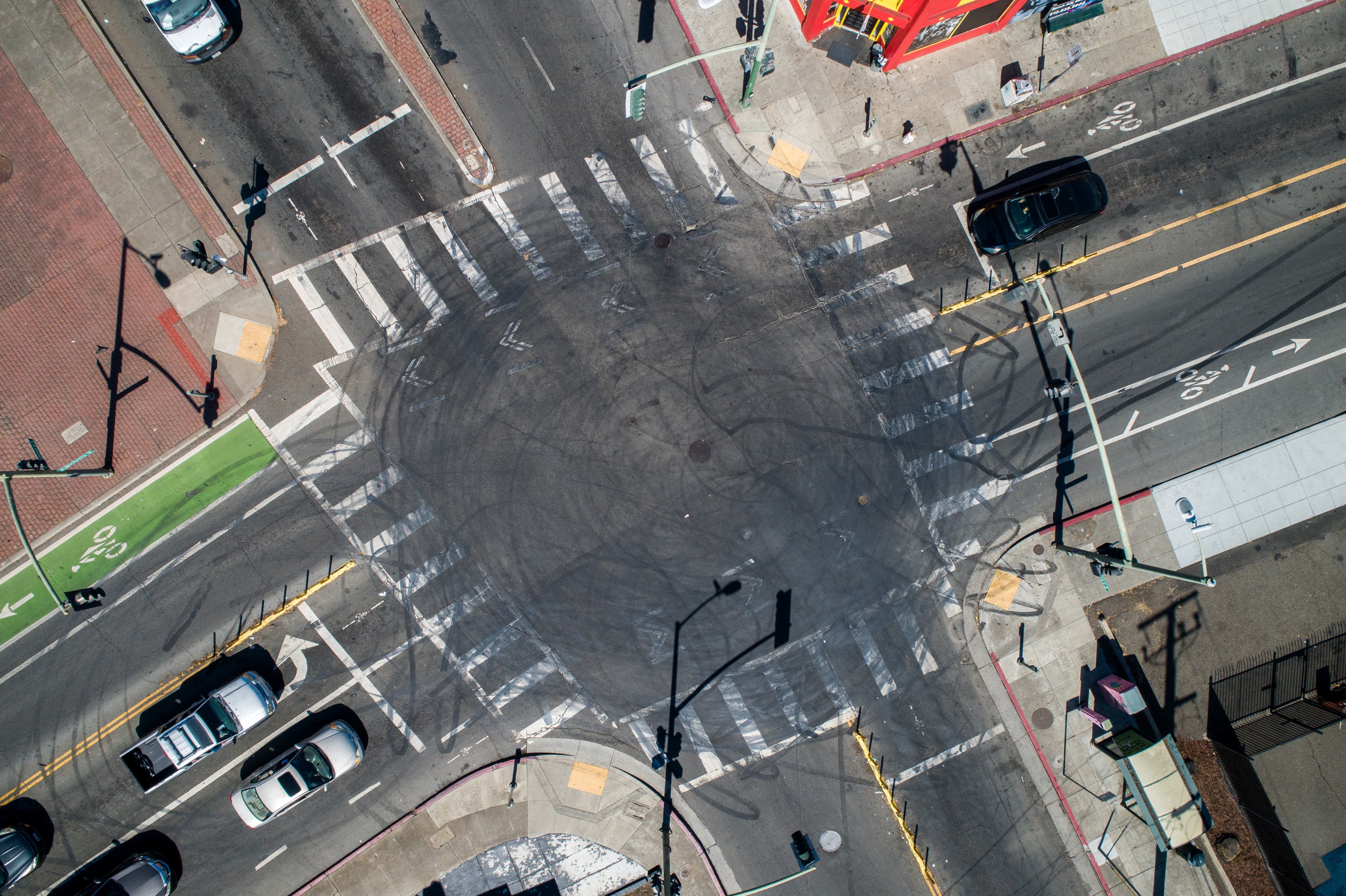 Aerial view of a busy intersection with multiple crosswalks, bike lanes, cars at stoplights, and a red building at the top. Skid marks are visible in the center.